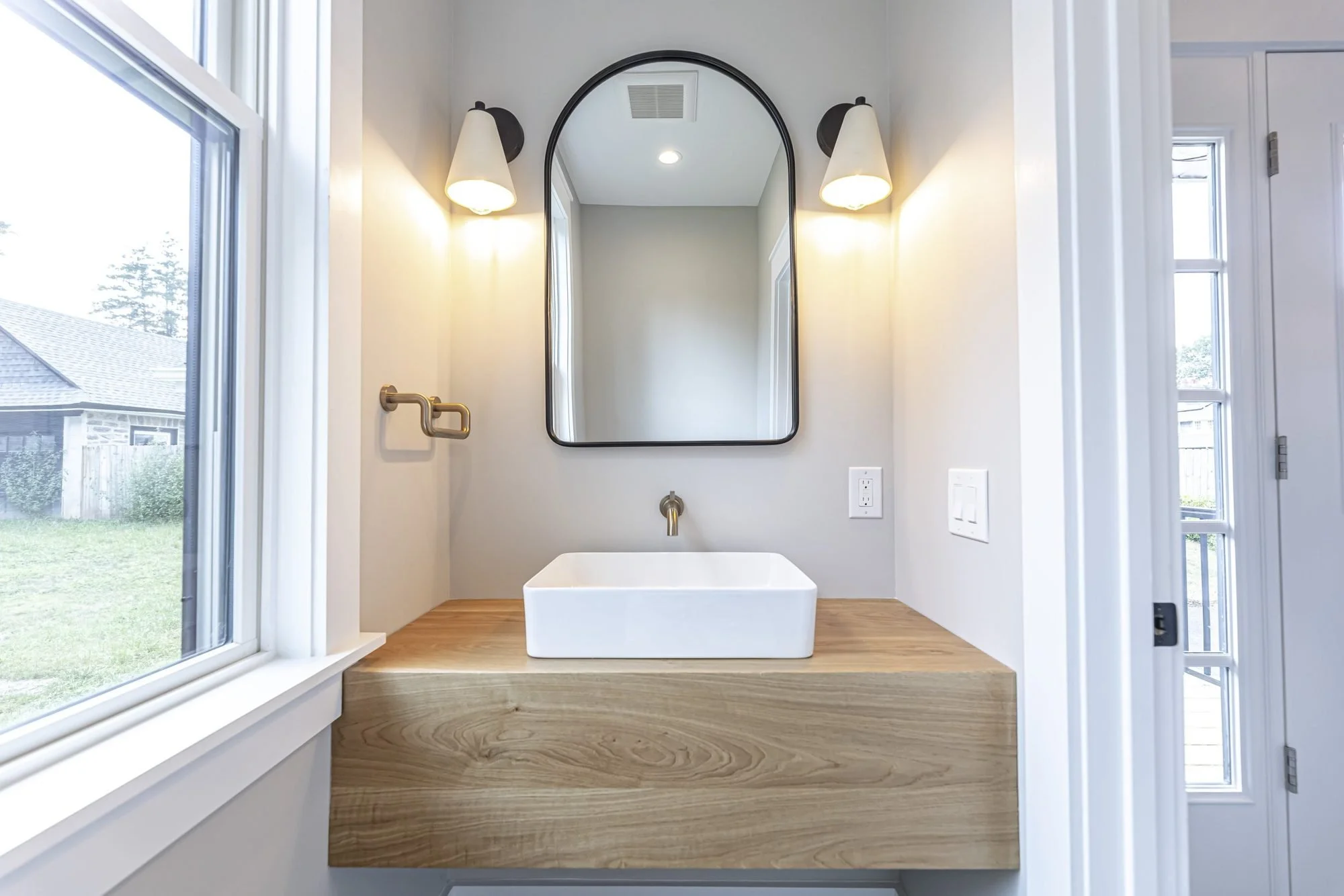 Powder room with floating oak vanity, vessel sink and arched mirror