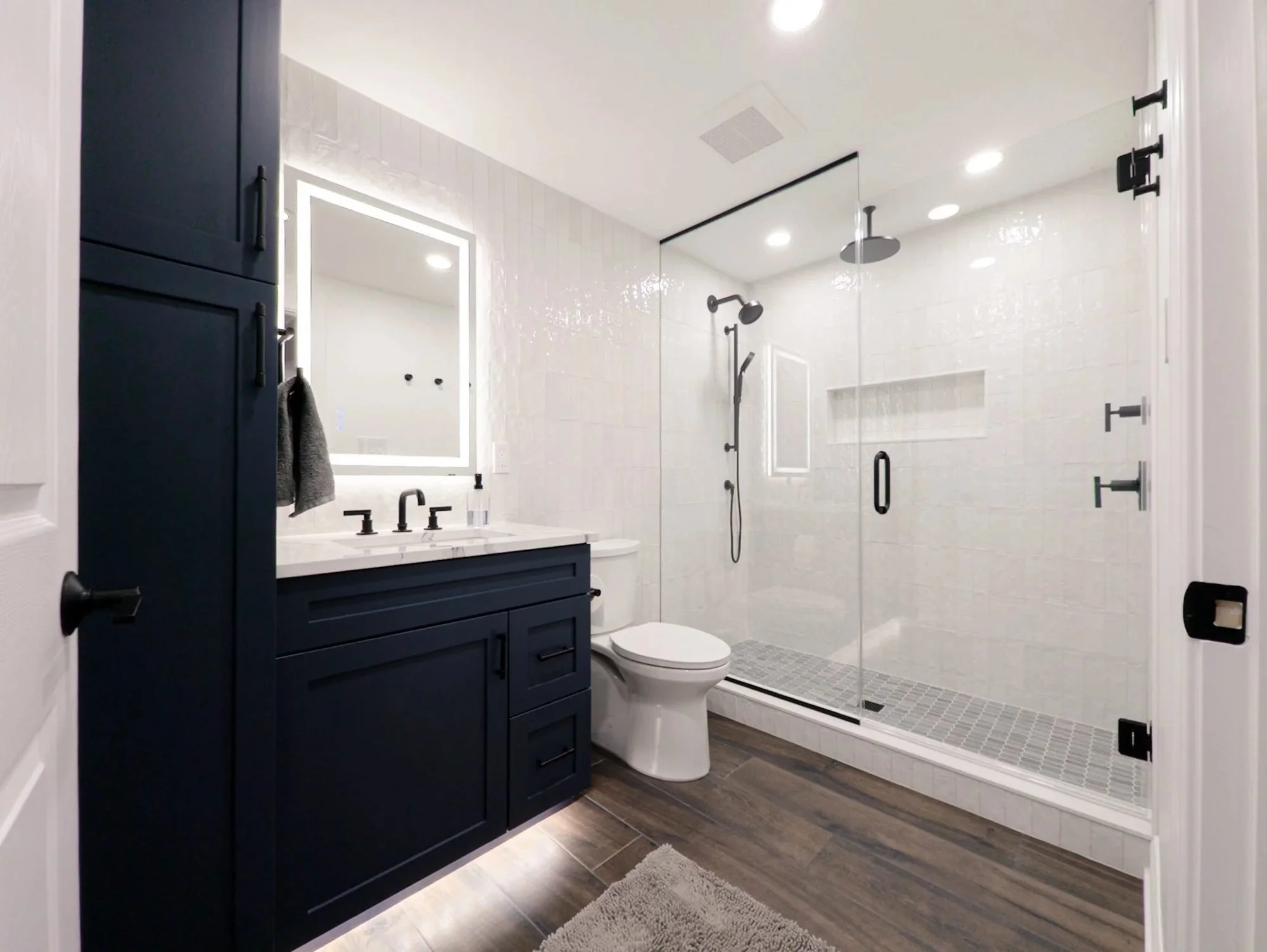 Basement bathroom with navy vanity, LED mirror and glass shower