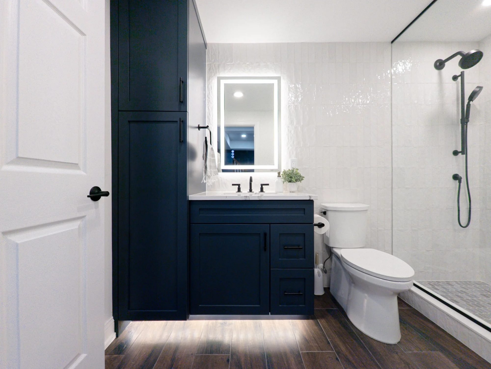 Basement bathroom with navy vanity, linen tower and backlit mirror
