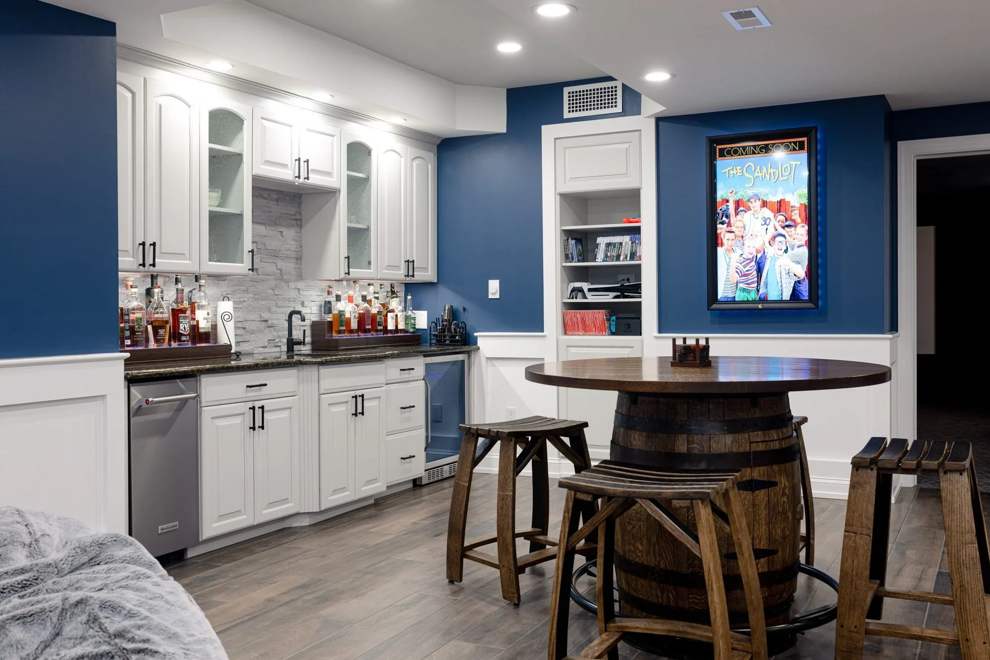Basement wet bar with white cabinets, barrel pub table and navy walls