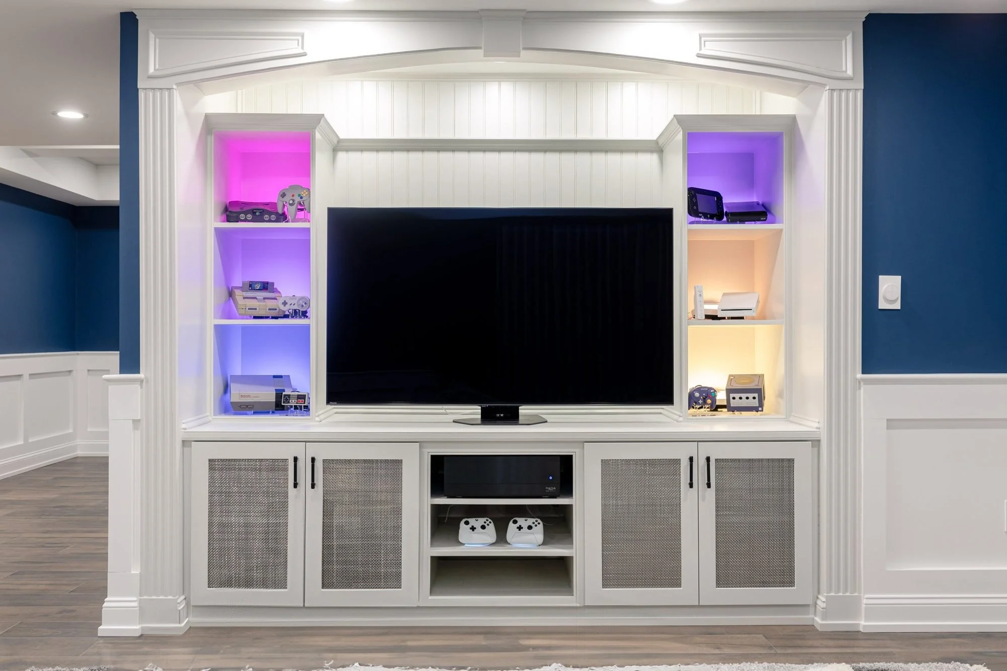 Basement media wall with white built-ins and LED-lit shelves