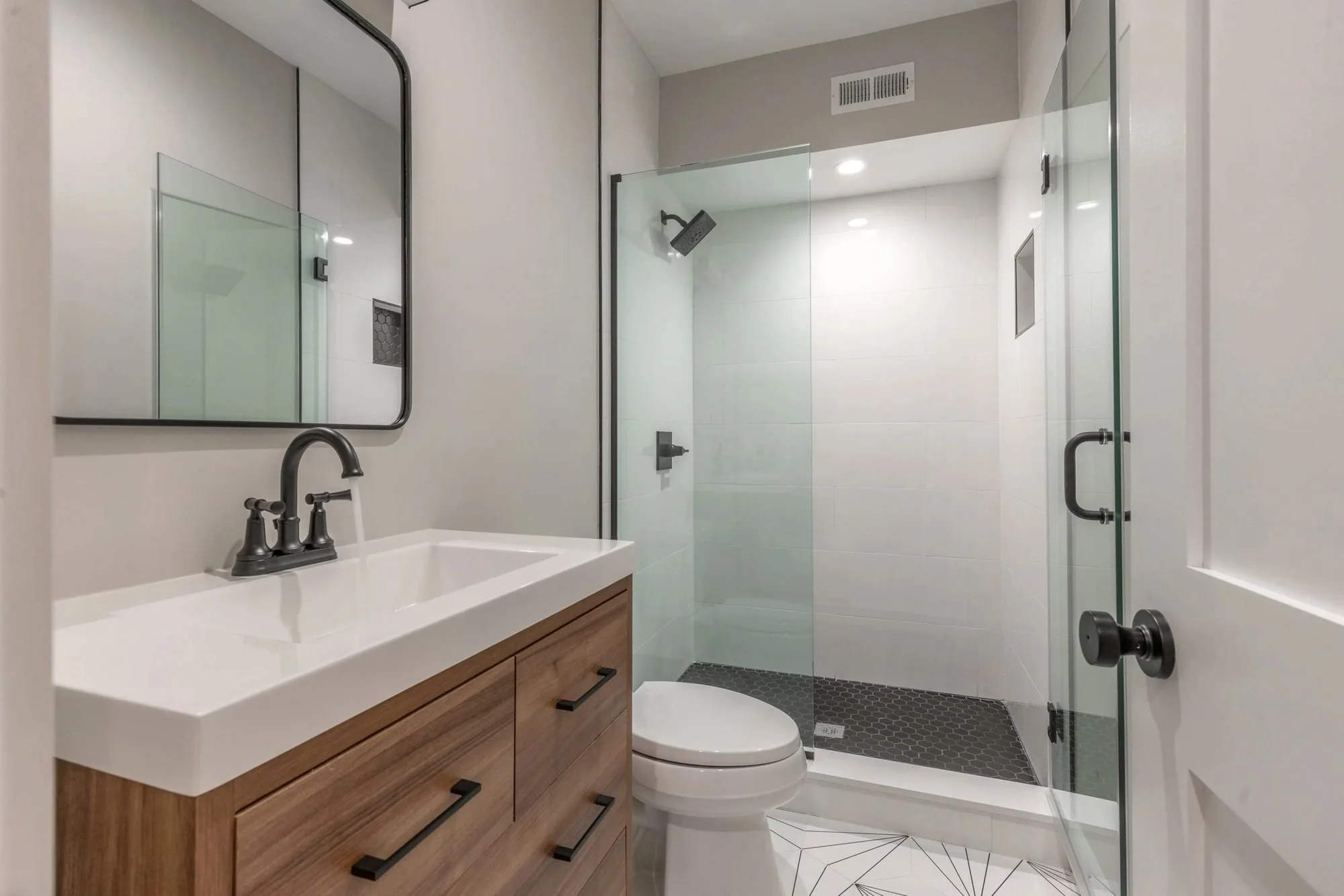Frameless glass shower and wood vanity with matte black faucet