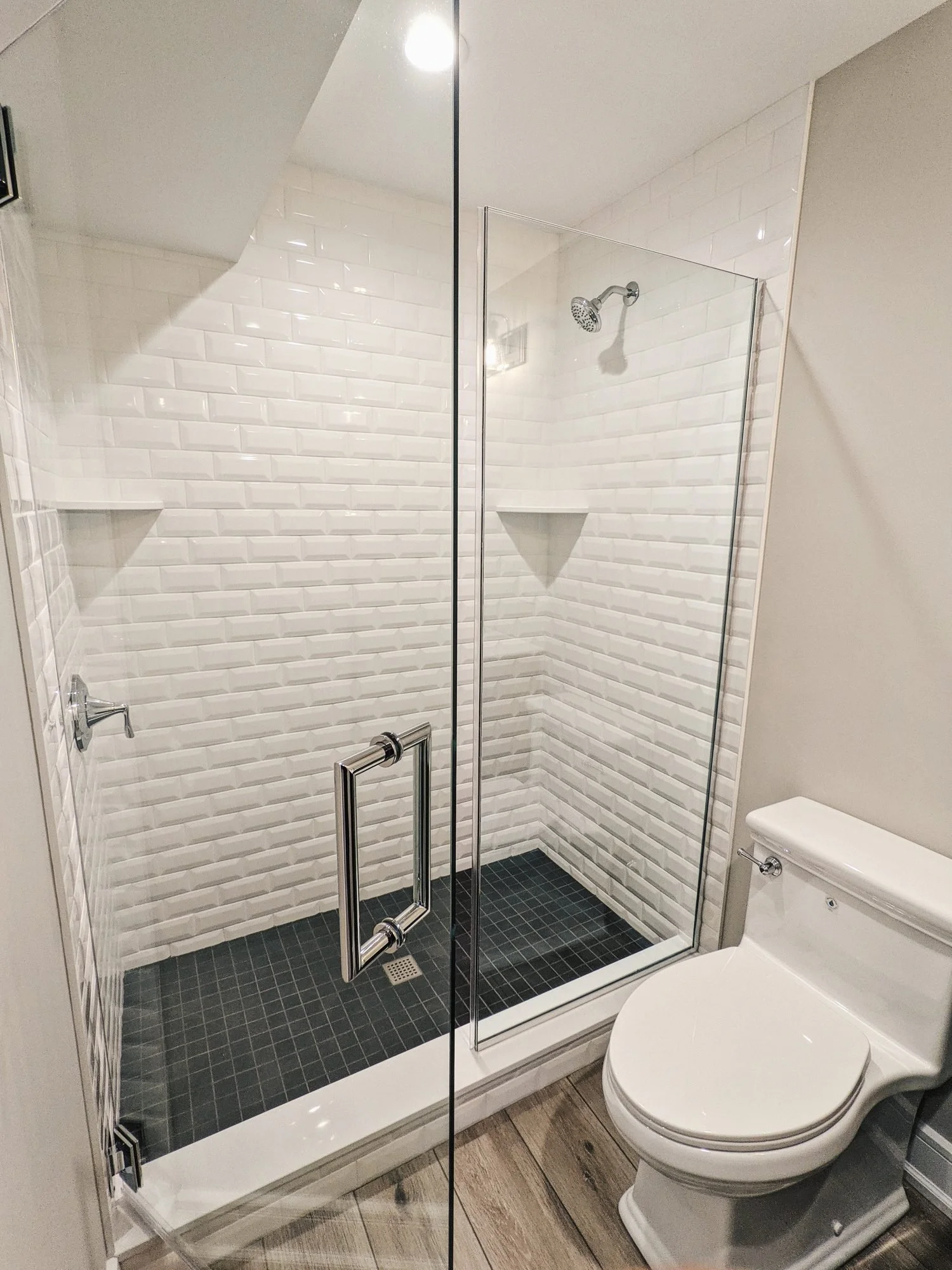 Basement shower with white beveled subway tile and black floor tile