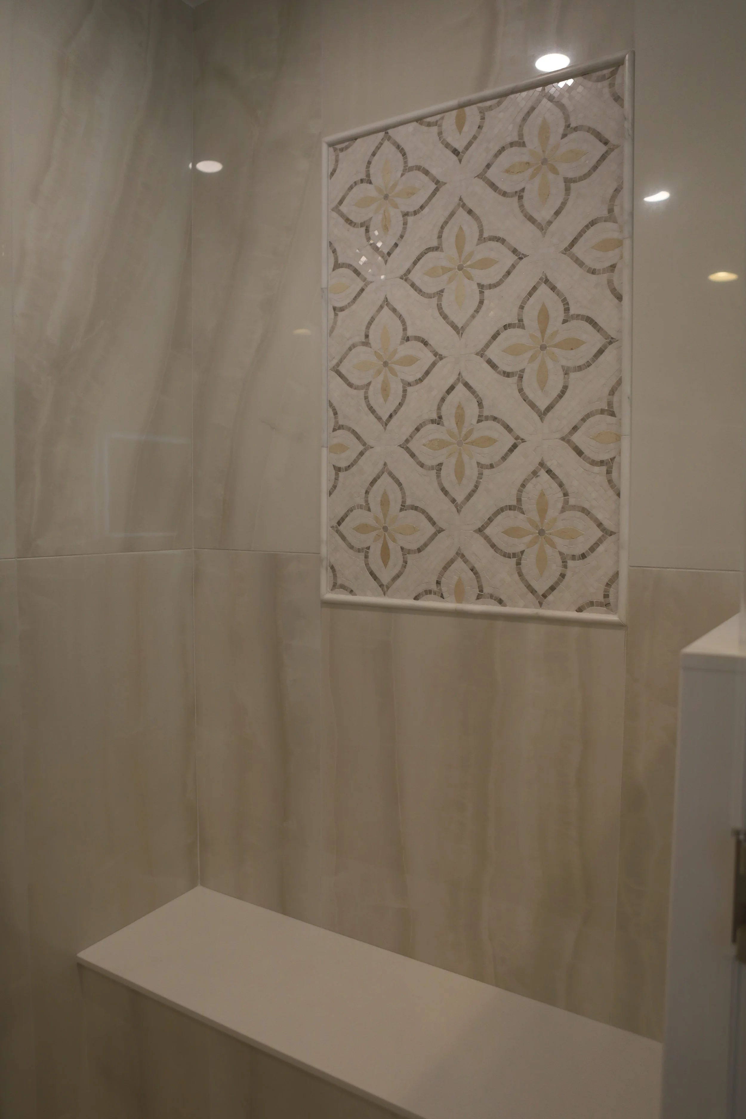Neutral walk-in shower with large-format tile and a decorative patterned tile niche.