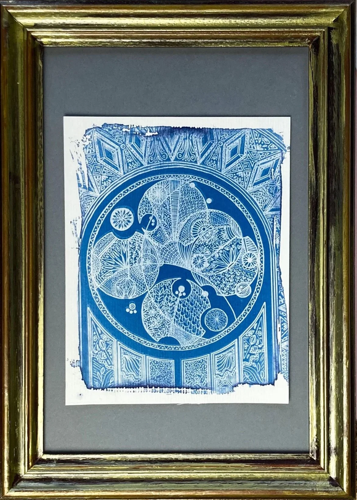 Une œuvre d'art en papier découpé de couleur bleue, encadrée dans un cadre en bois ancien. La sculpture présente des motifs géométriques et floraux compliqués, avec un cercle central et divers détails décoratifs.