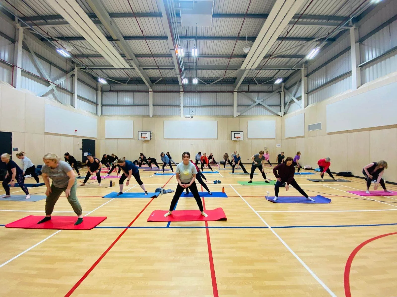 Group of people participating in a fitness class in a gymnasium, using exercise mats for stretching or yoga.