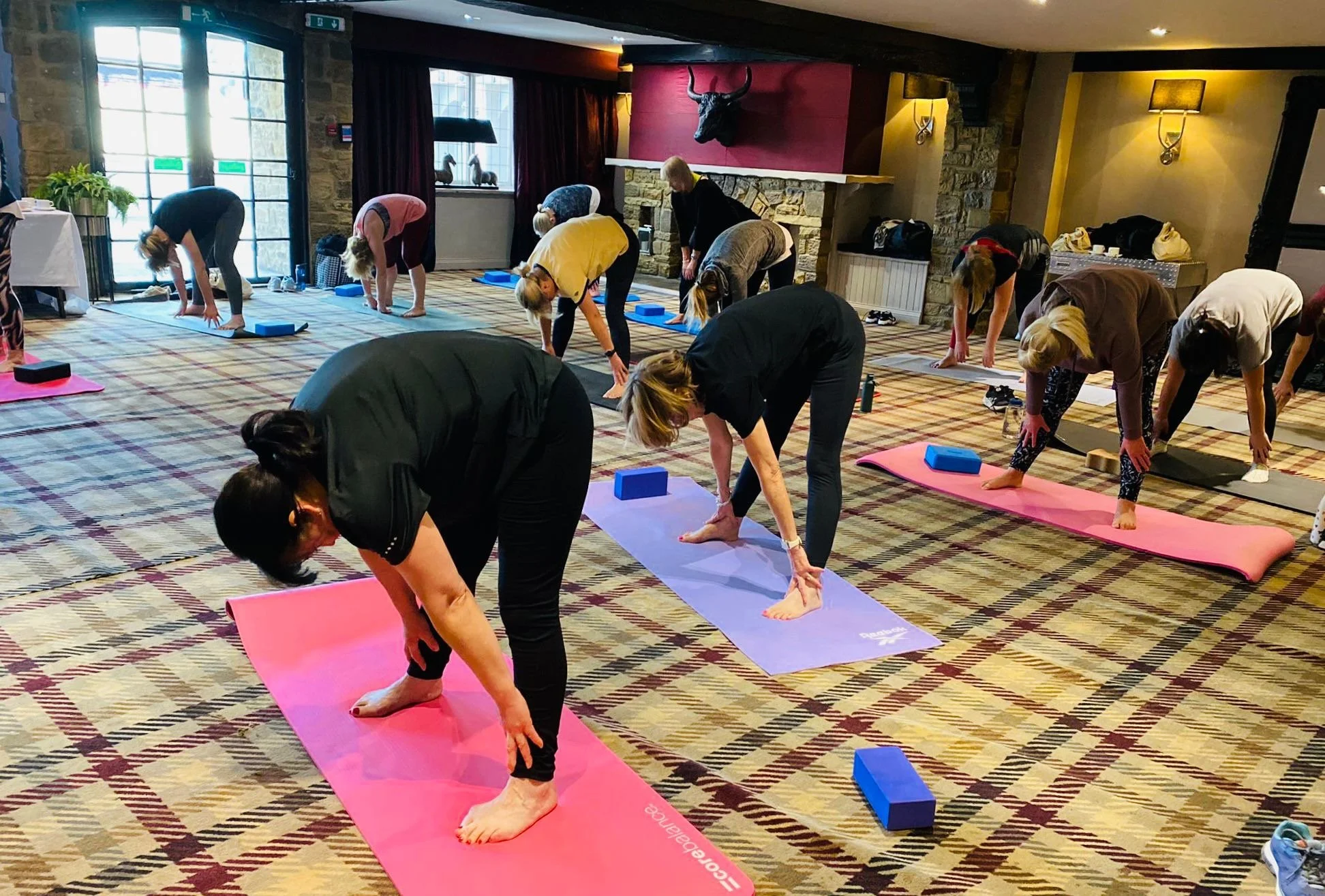 Group of women participating in a yoga class in a room with large windows, stone walls, and a red wall with a mounted bull skull