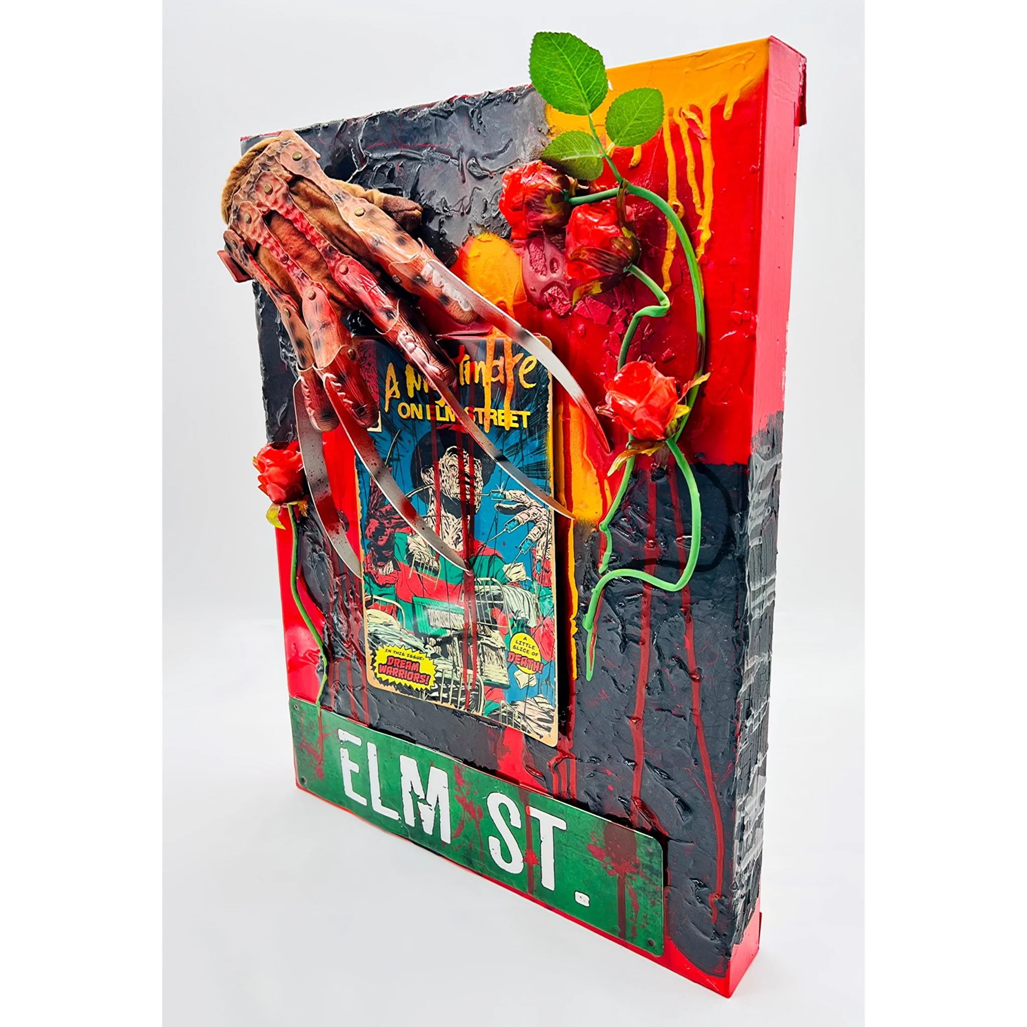 Mixed media artwork featuring a comic book cover with red, green, and black paint, green vines with red roses, and a metallic hand sculpture.