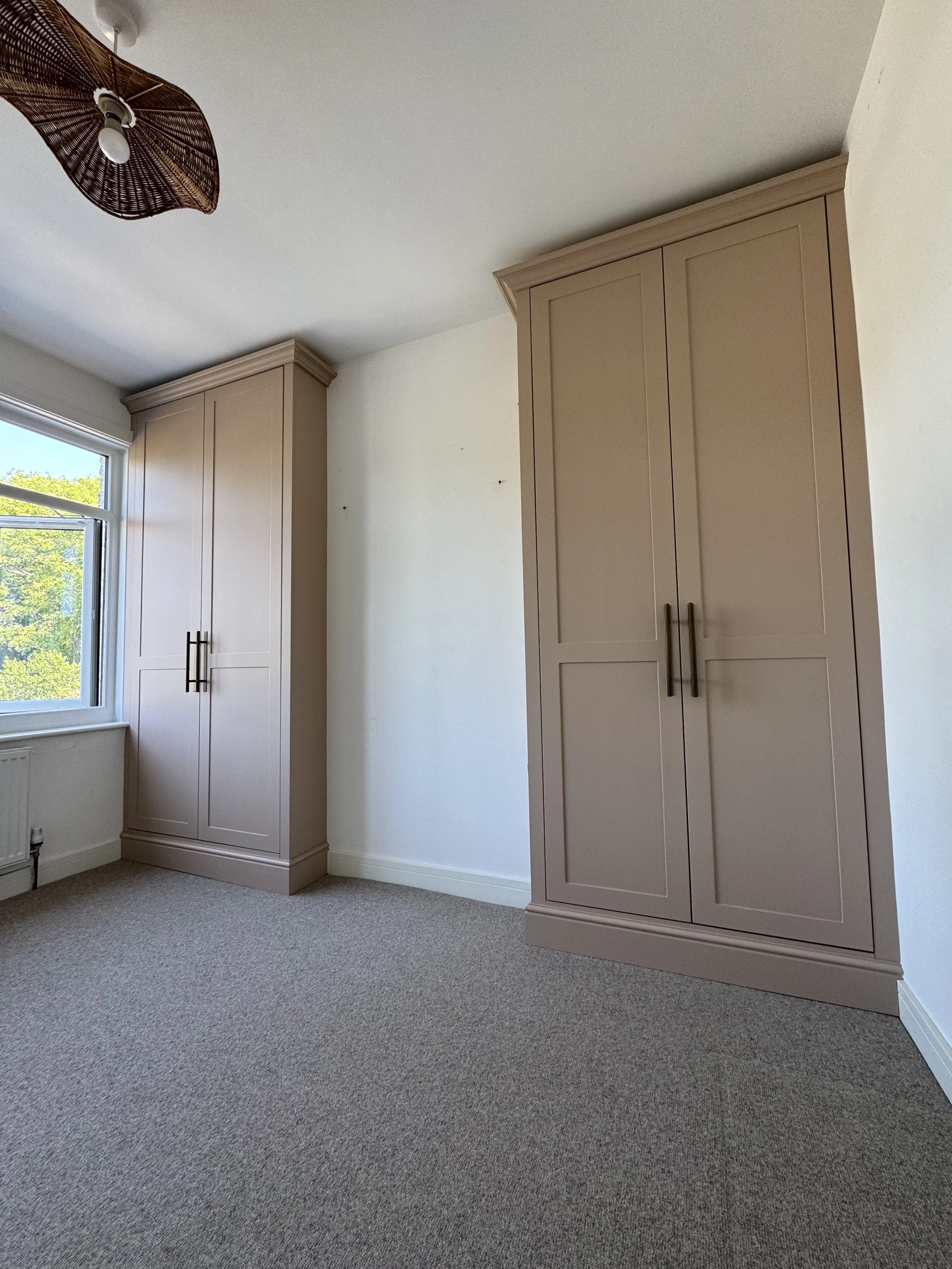 Interior of a room with beige cabinetry, a window, and a beige carpeted floor.