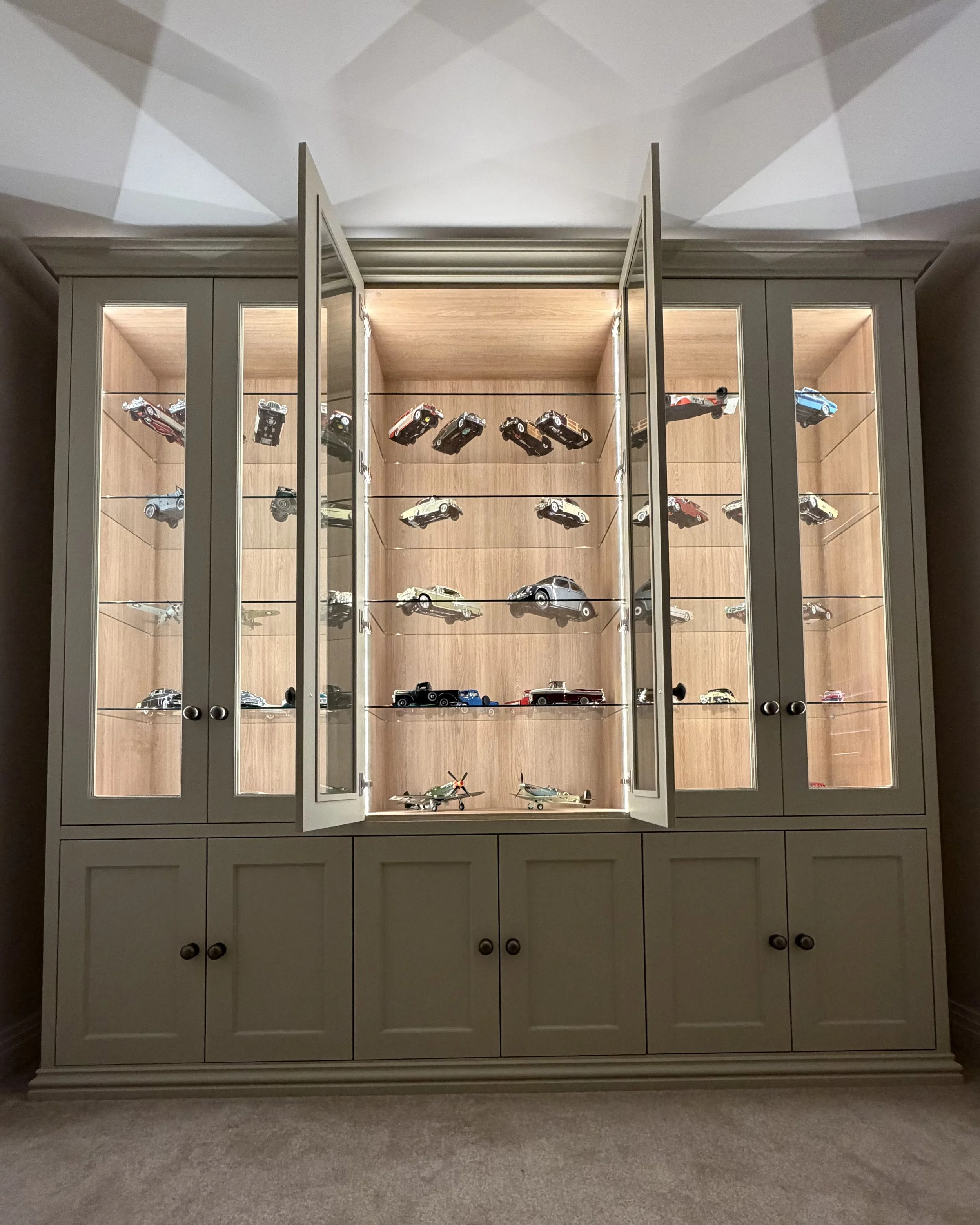 Display cabinet with glass doors filled with model cars and airplanes.