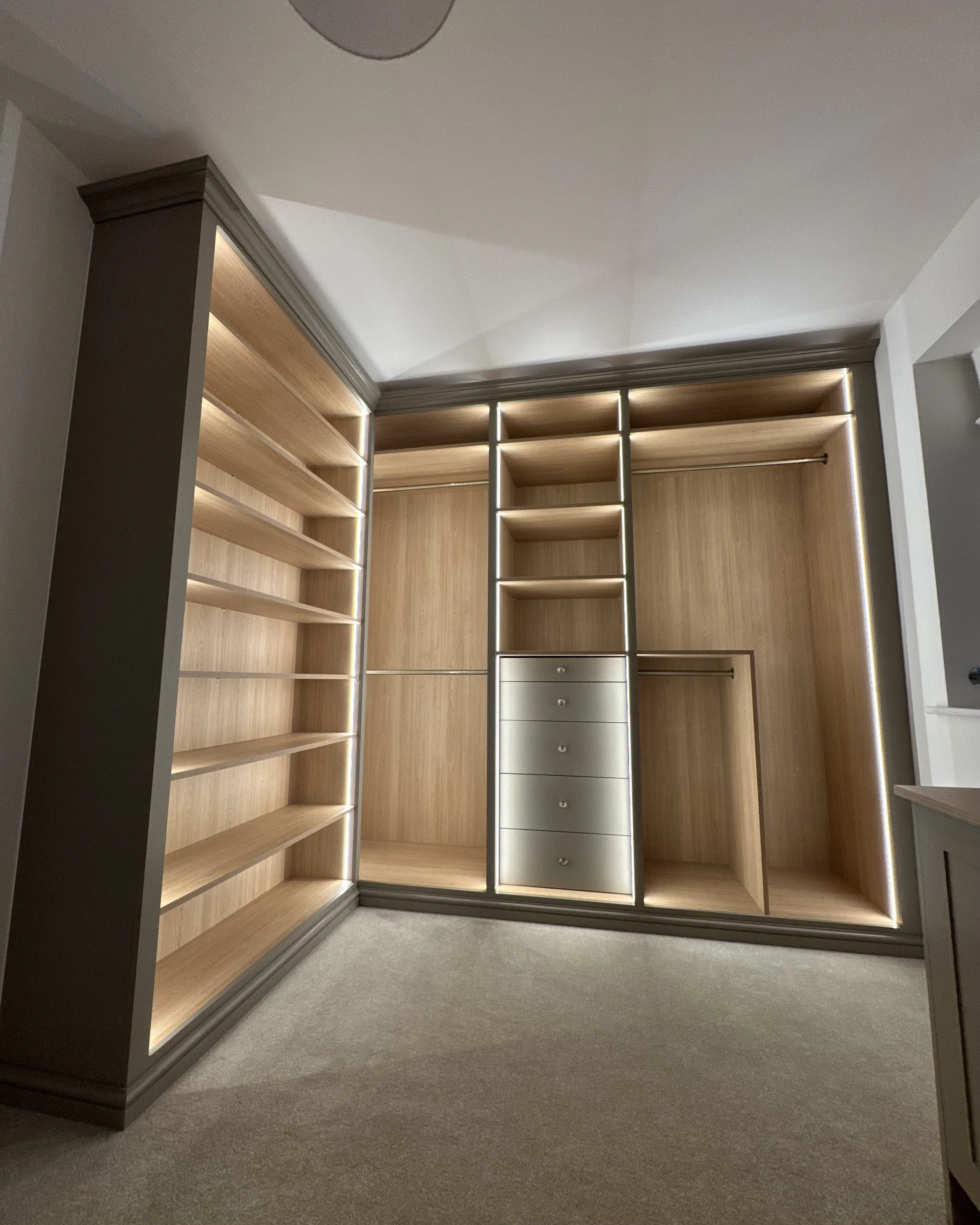 Empty wooden closet with built-in shelves and drawers, beige carpeted floor, and ceiling light fixture.