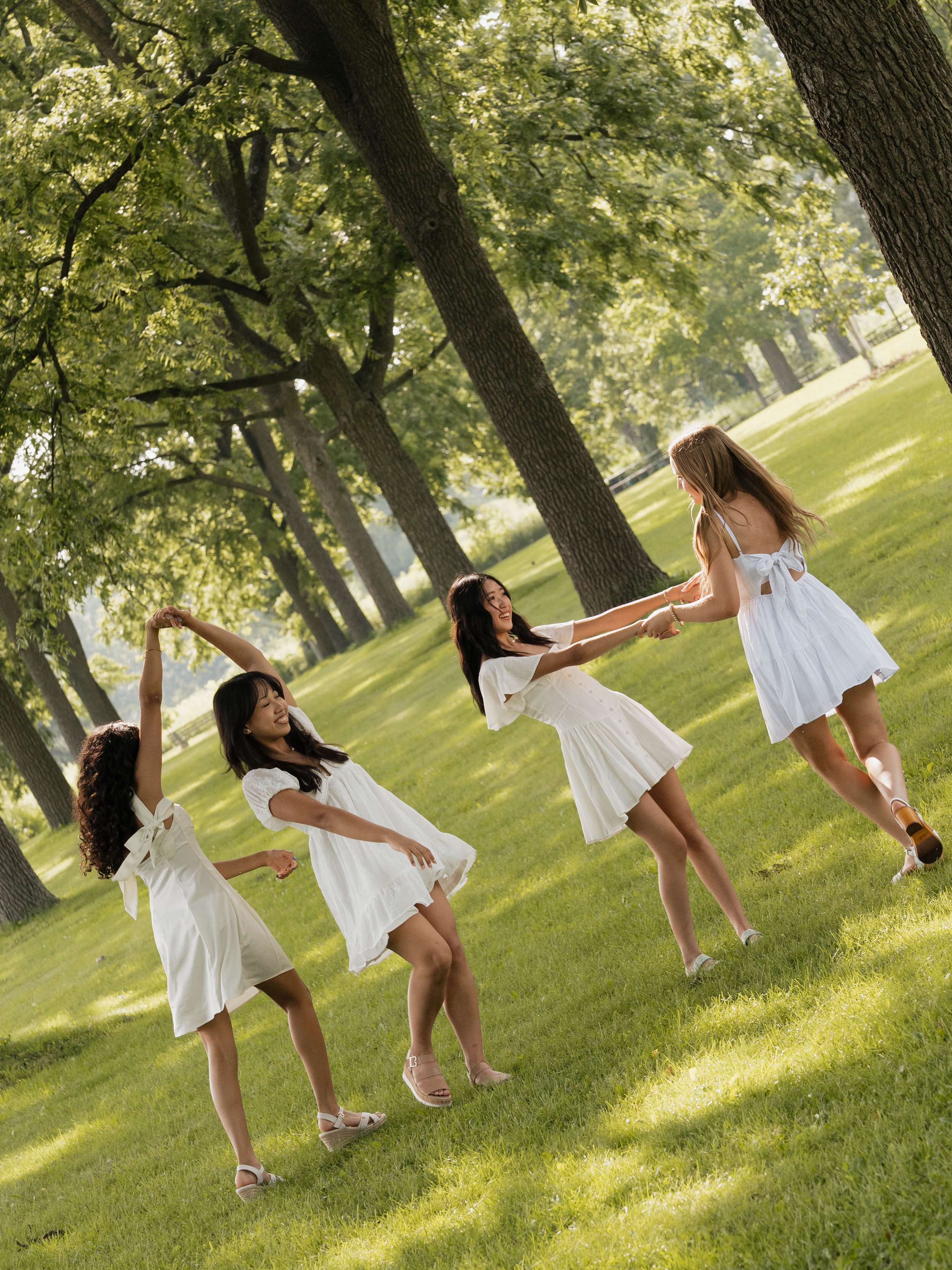 Two women sitting on grass, embracing and smiling, with buildings in the background.