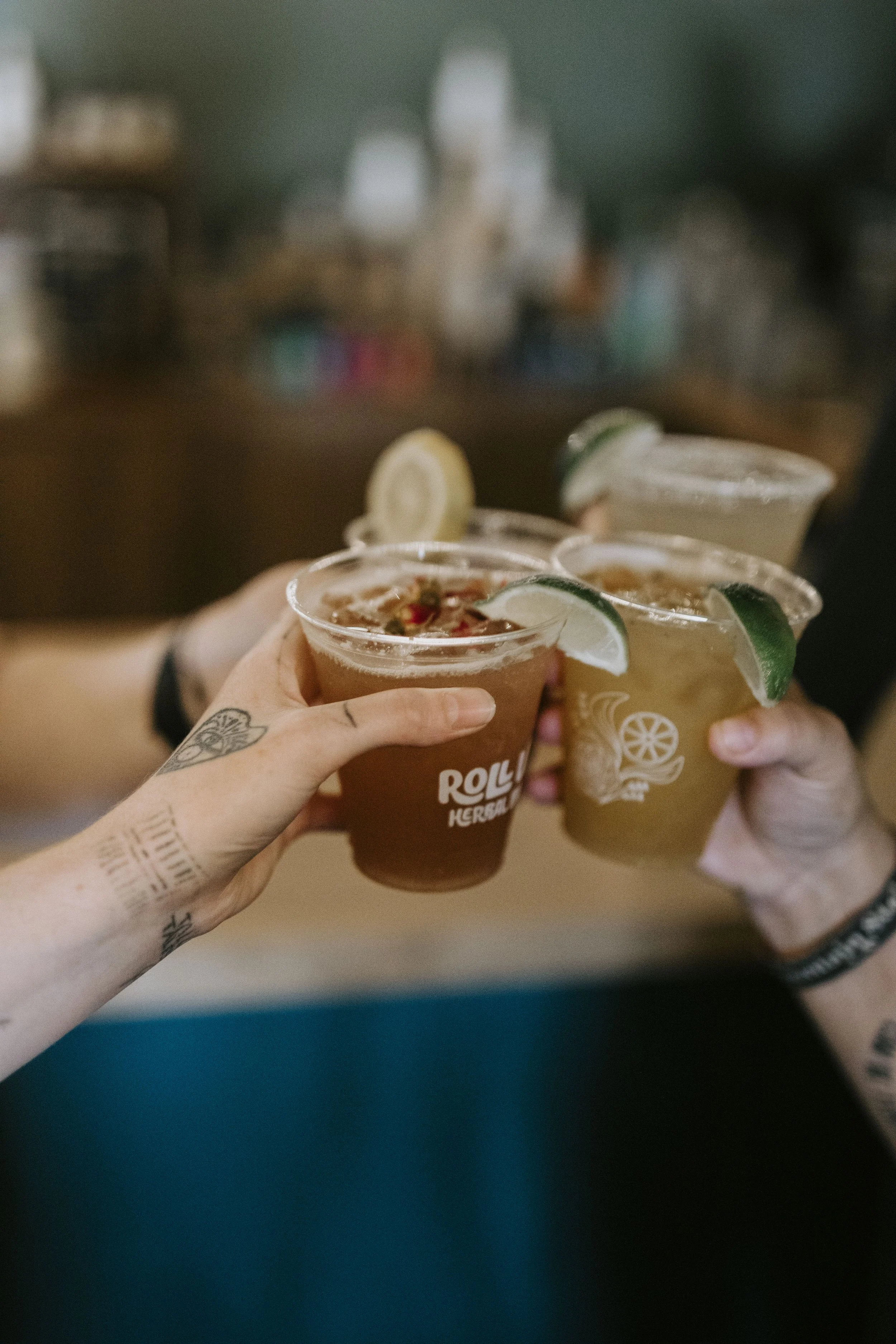 Four people holding cocktails garnished with lime wedges, with blurred background of a bar or restaurant setting.