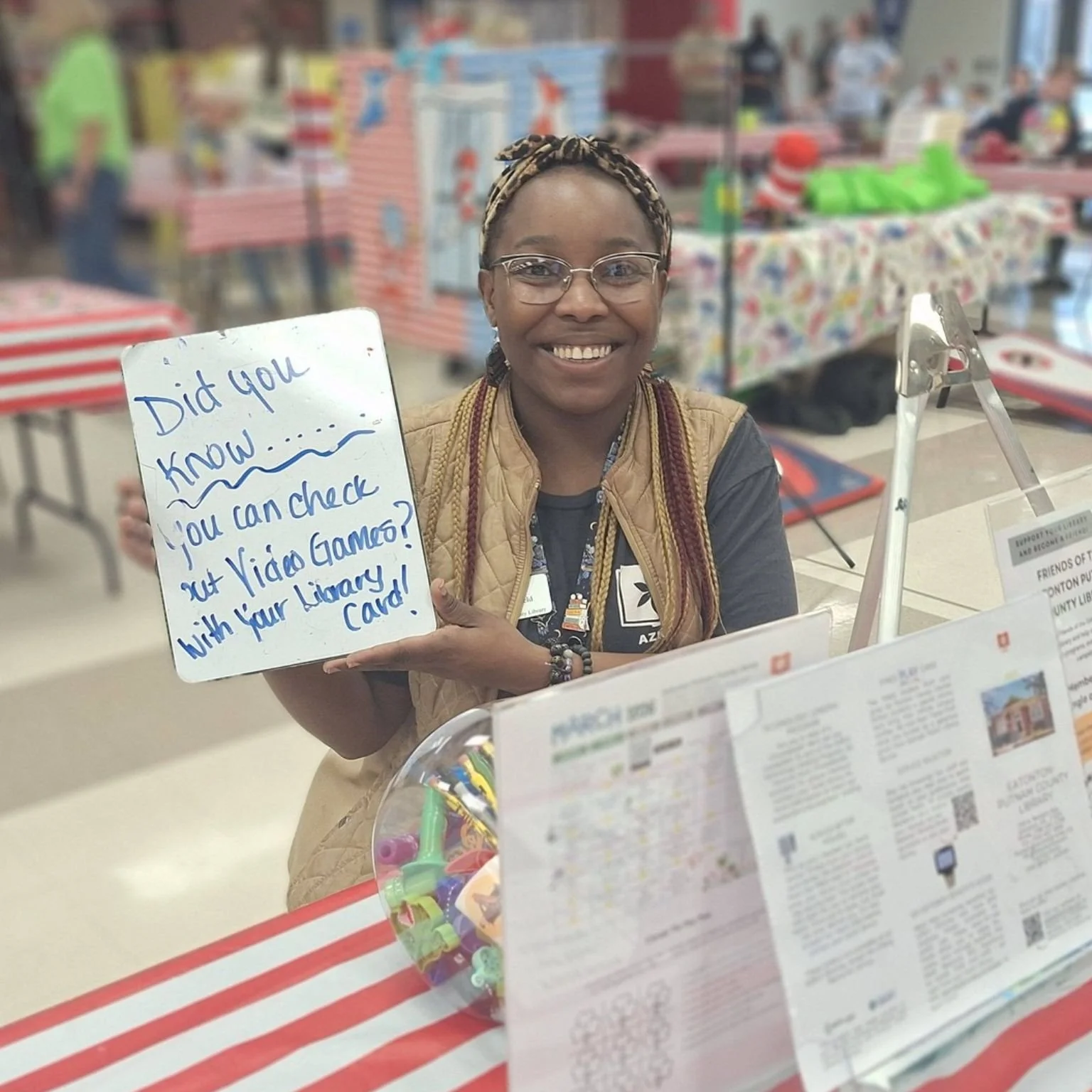 Abby Boatfield, Eatonton-Putnam County Library Manager, holding a whiteboard reading, "Did you know... you can check out Video Games? with your Library Card!" at an event table.