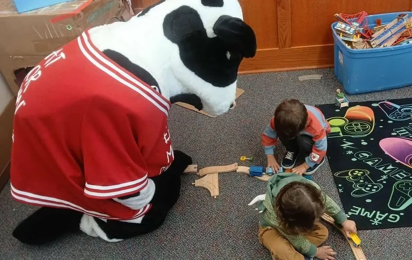 Chickfila Oconee Cow playing trains with young children at the library