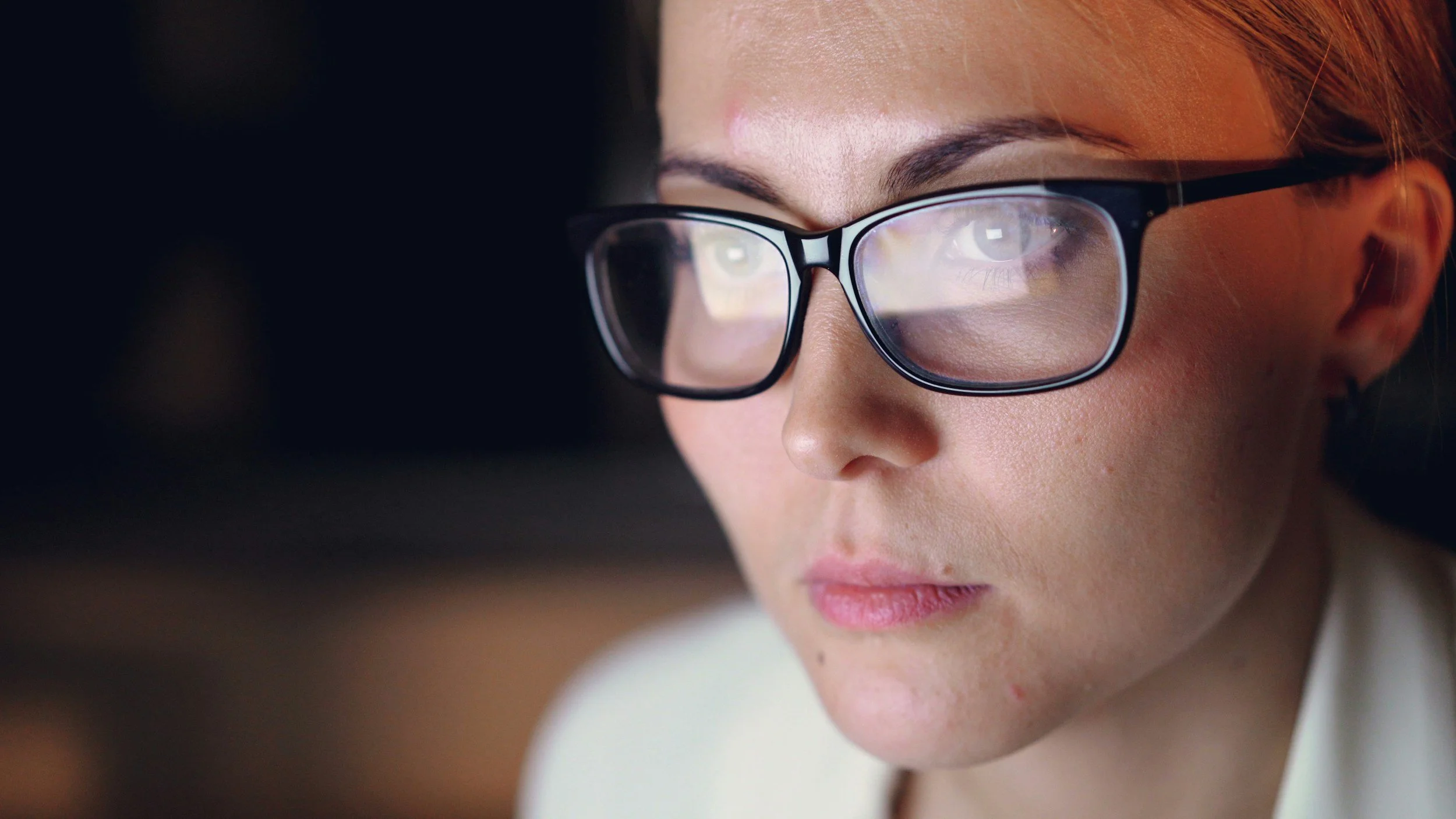 Close-up of a woman with glasses focused on a screen.