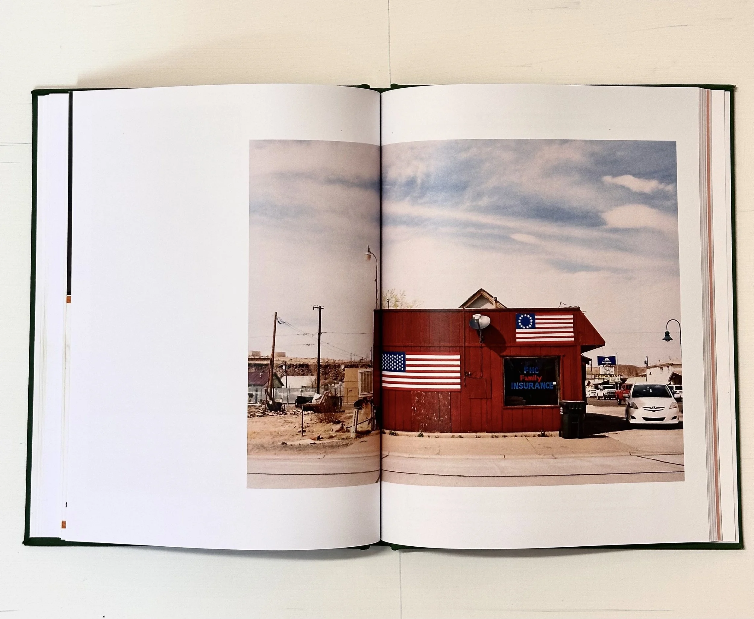 A small red building with Americana flags painted on the exterior and signage indicating it is an insurance office in a rural area, with cars parked nearby and power lines in the background.