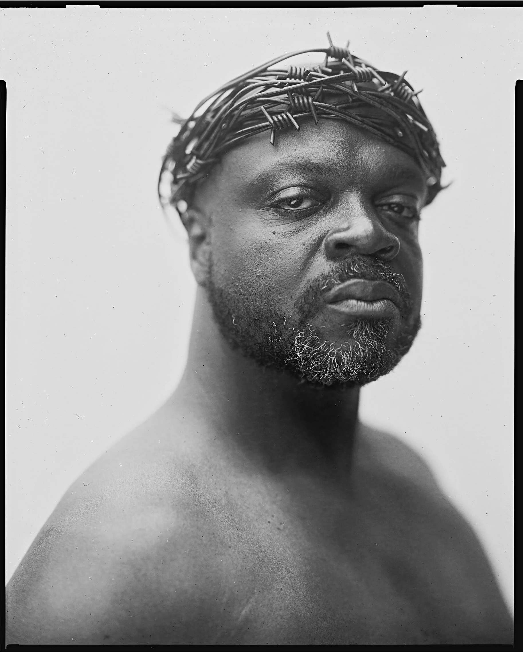 Fine art black and white large format portrait of a man wearing a crown made of barbed wire by Parker J Pfister