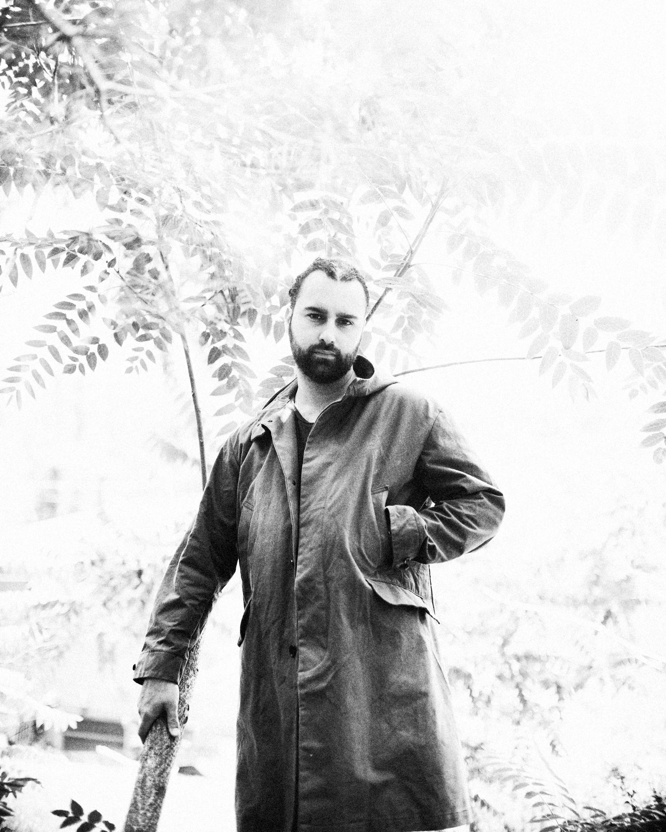 Black and white full-length portrait of musical artist I Give My Friends Flowers standing in a coat holding a cane outdoors, created for his album Dog Star, photographed by Parker J. Pfister.