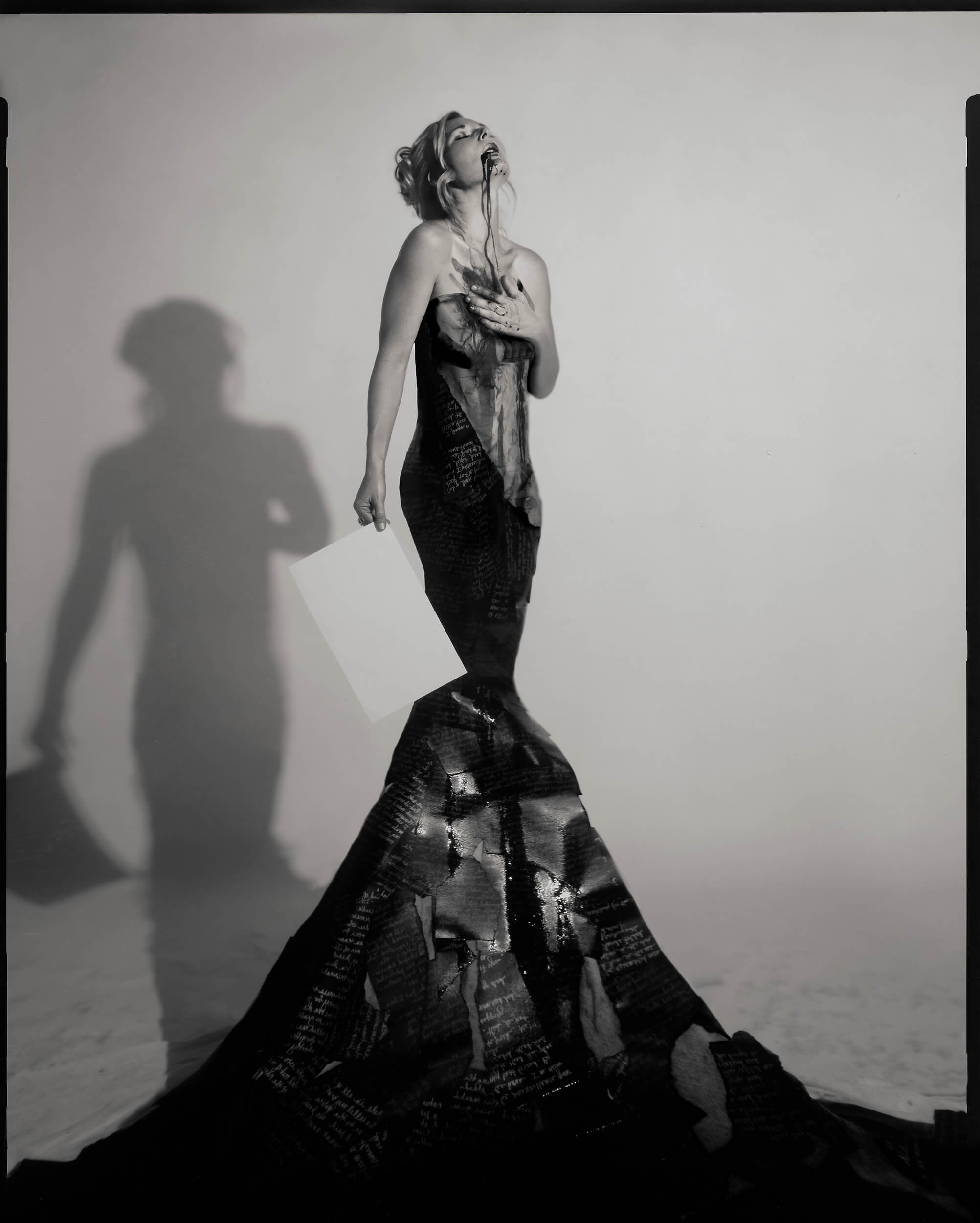 Parker J Pfister Fine Art Black and White Constraint Portrait of a white woman in a large flowing ballgown holding a piece of white paper and has blood running out of her mouth.
