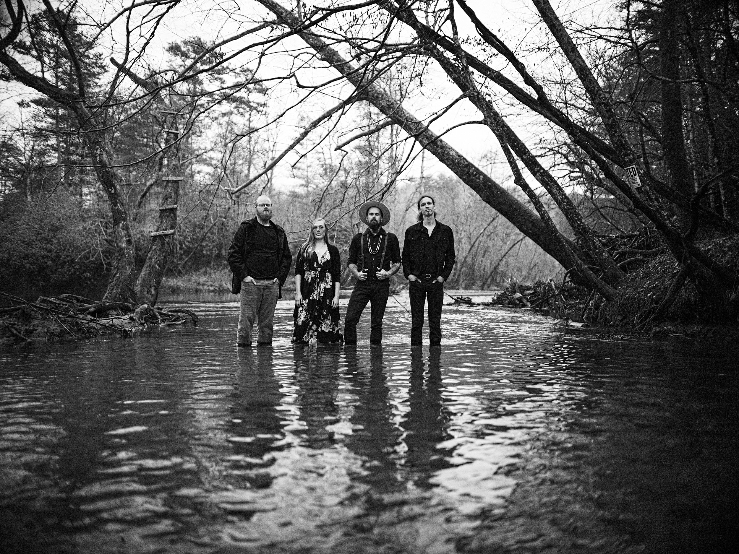Black and white environmental portrait of the band Life Like Water standing knee-deep in a calm river, photographed in North Carolina by Parker J. Pfister.