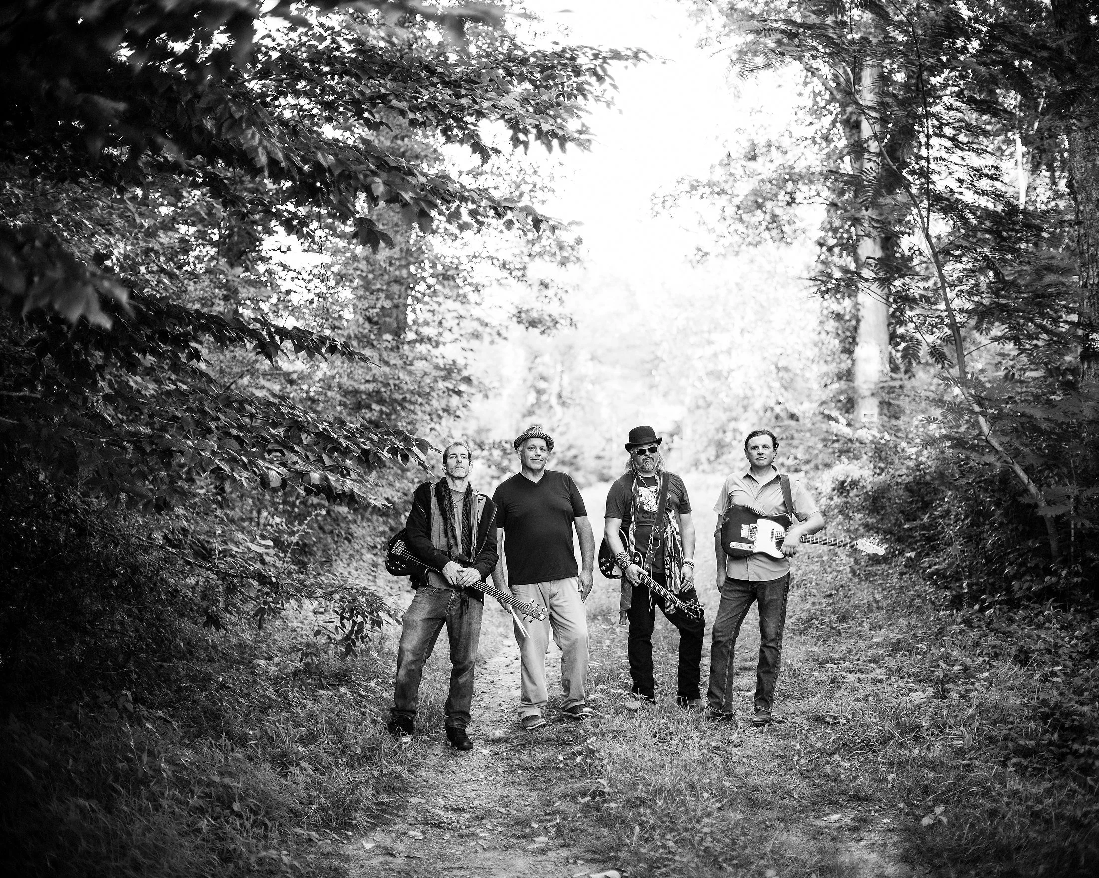 Black and white group portrait of Western North Carolina Southern rock band Velvet Truckstop standing together outdoors on a wooded path, photographed by Parker J. Pfister.