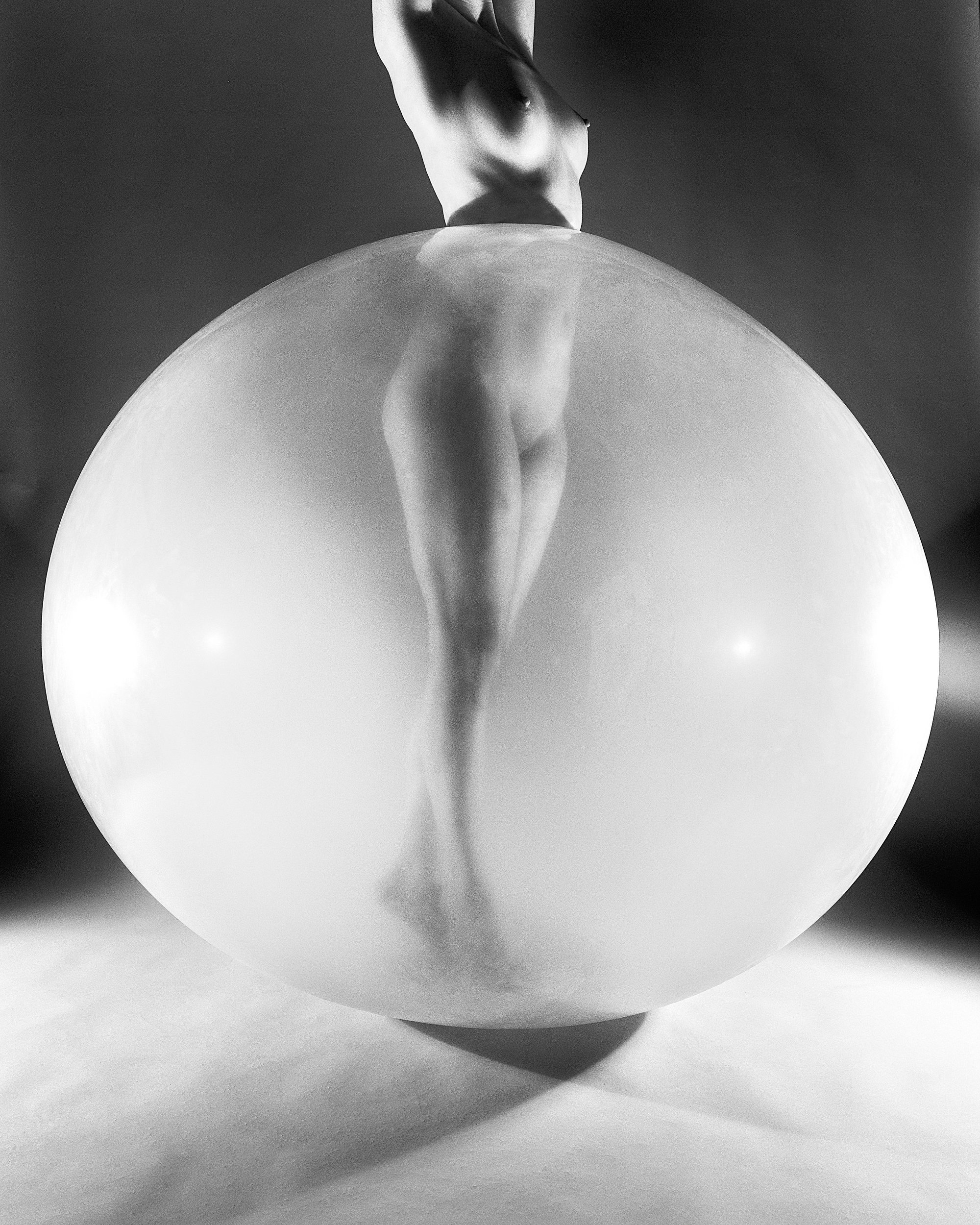 An abstract monochrome fine art nude figure study focusing on the curves of the human torso aligned perfectly with a large, glowing transparent sphere.