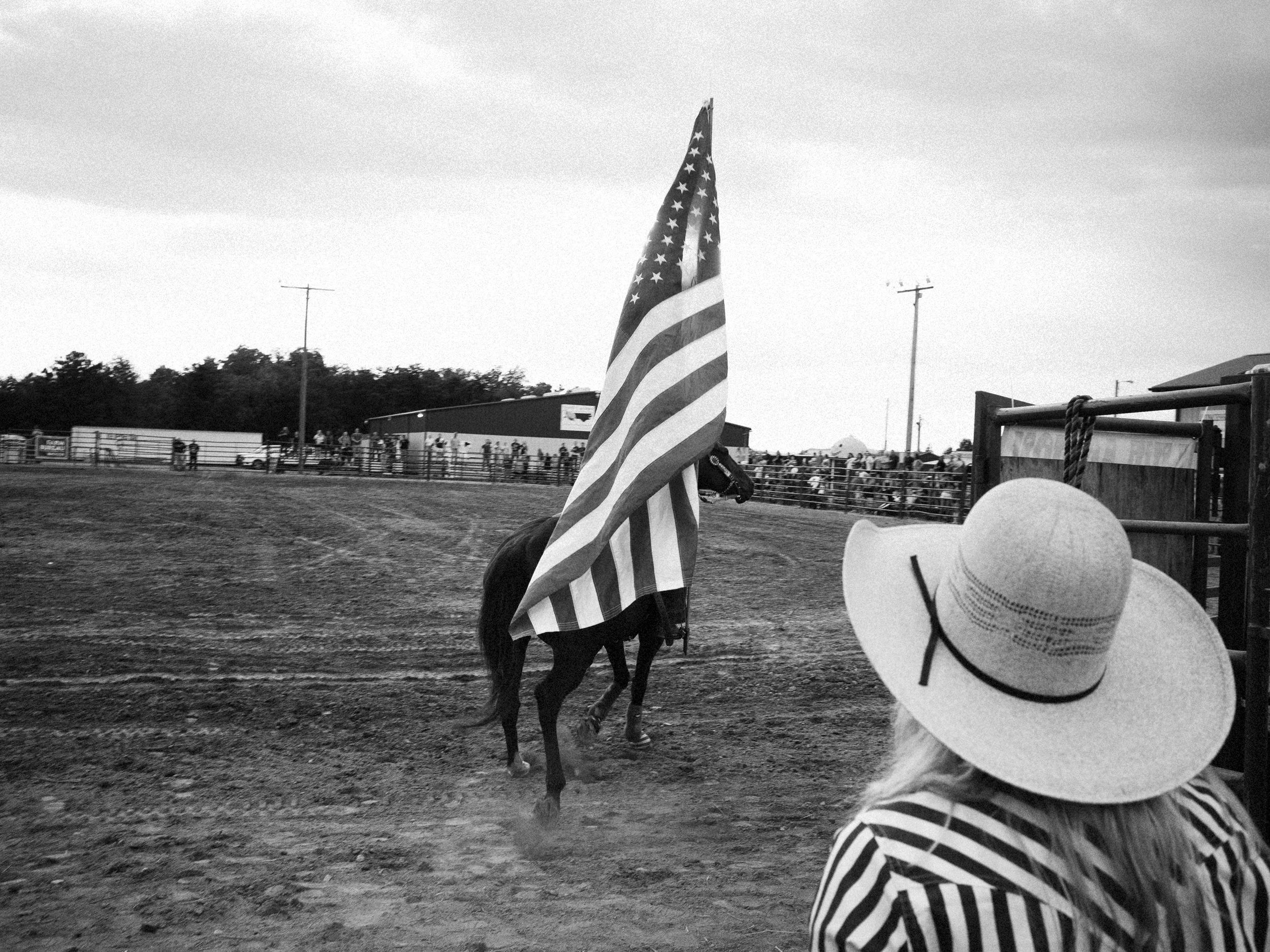 A gritty, first-person documentary photograph from a rodeo in Madison County, North Carolina, capturing the unvarnished characters and fleeting motion behind the chutes.