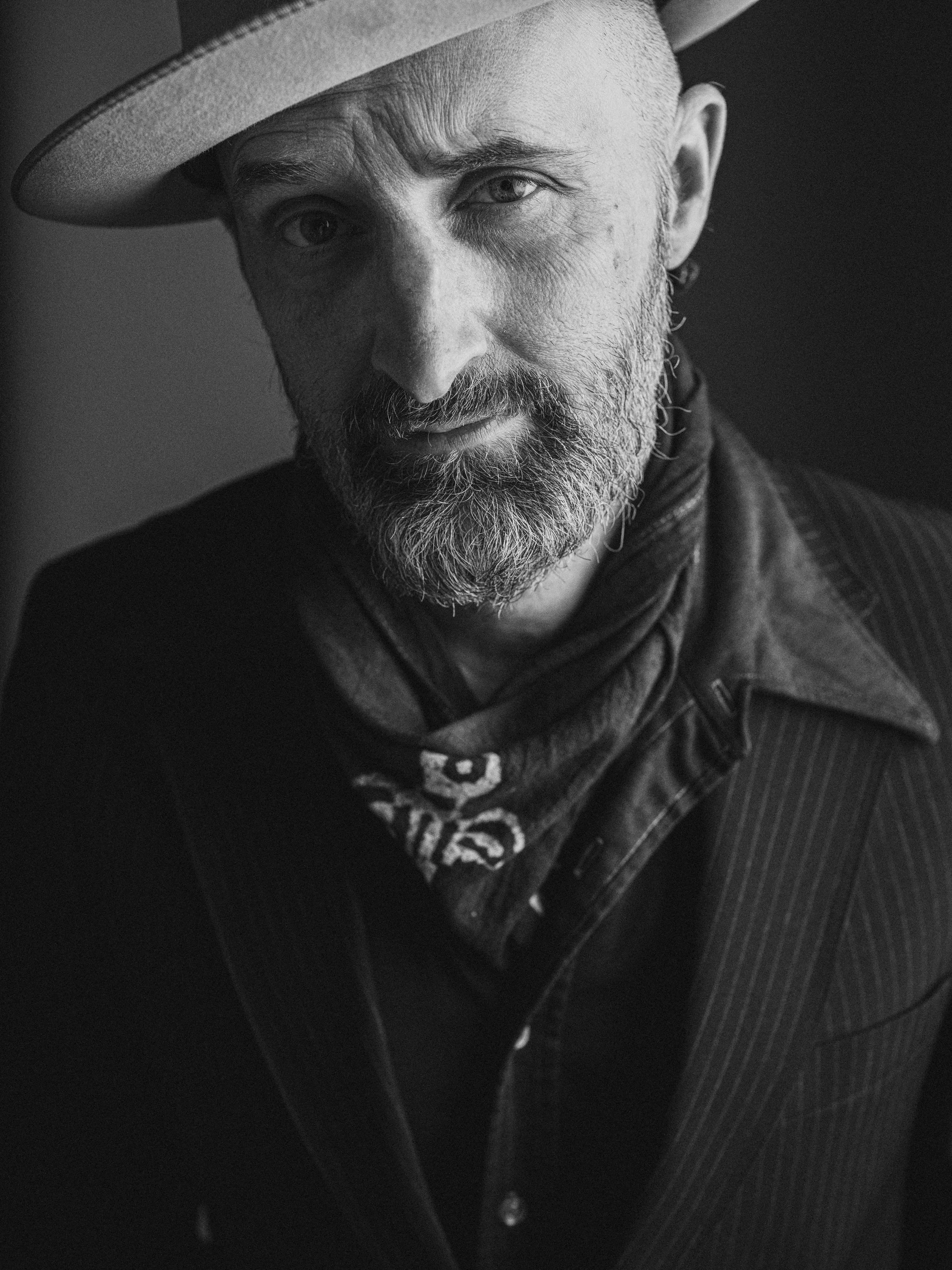 Intimate black and white portrait of blues singer-songwriter Seth Walker wearing a fedora, bandana, and suit jacket, photographed by Parker J. Pfister.