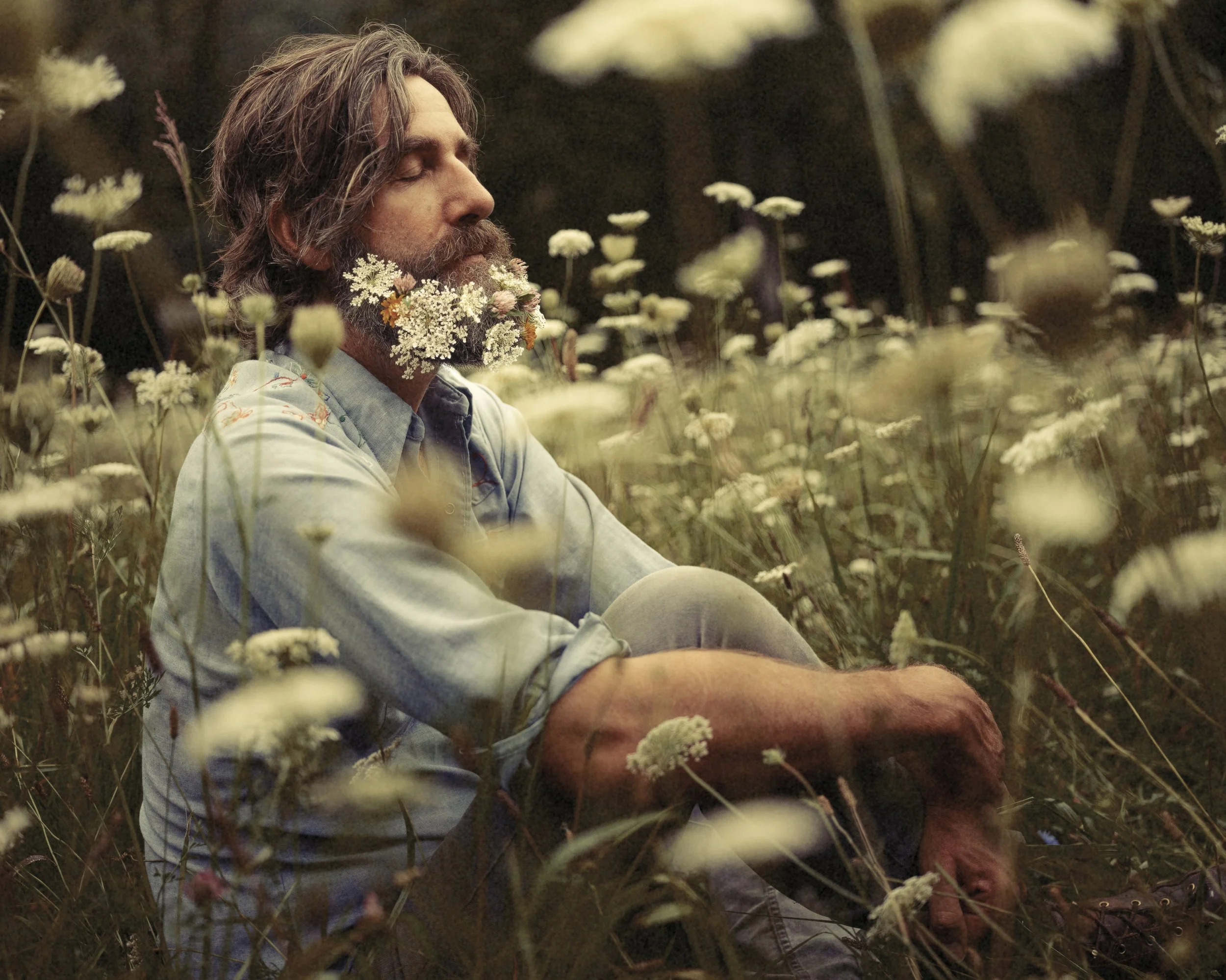 Warm outdoor portrait of singer-songwriter Tyler Ramsey lounging in a field of wildflowers, photographed by Parker J. Pfister.