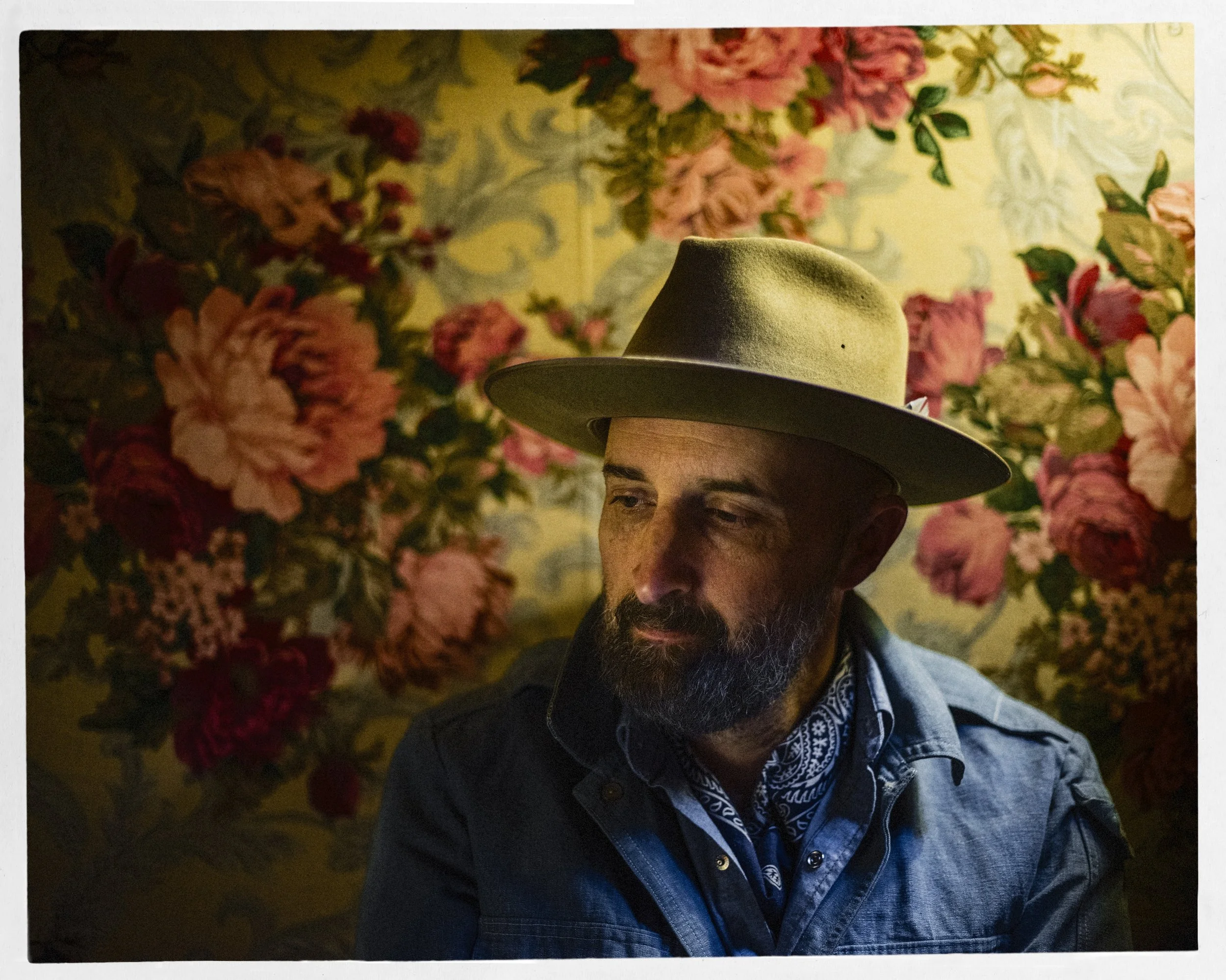 Warm color fine art portrait of blues singer-songwriter Seth Walker wearing a wide-brimmed hat framed against a vibrant floral background, photographed by Parker J. Pfister.