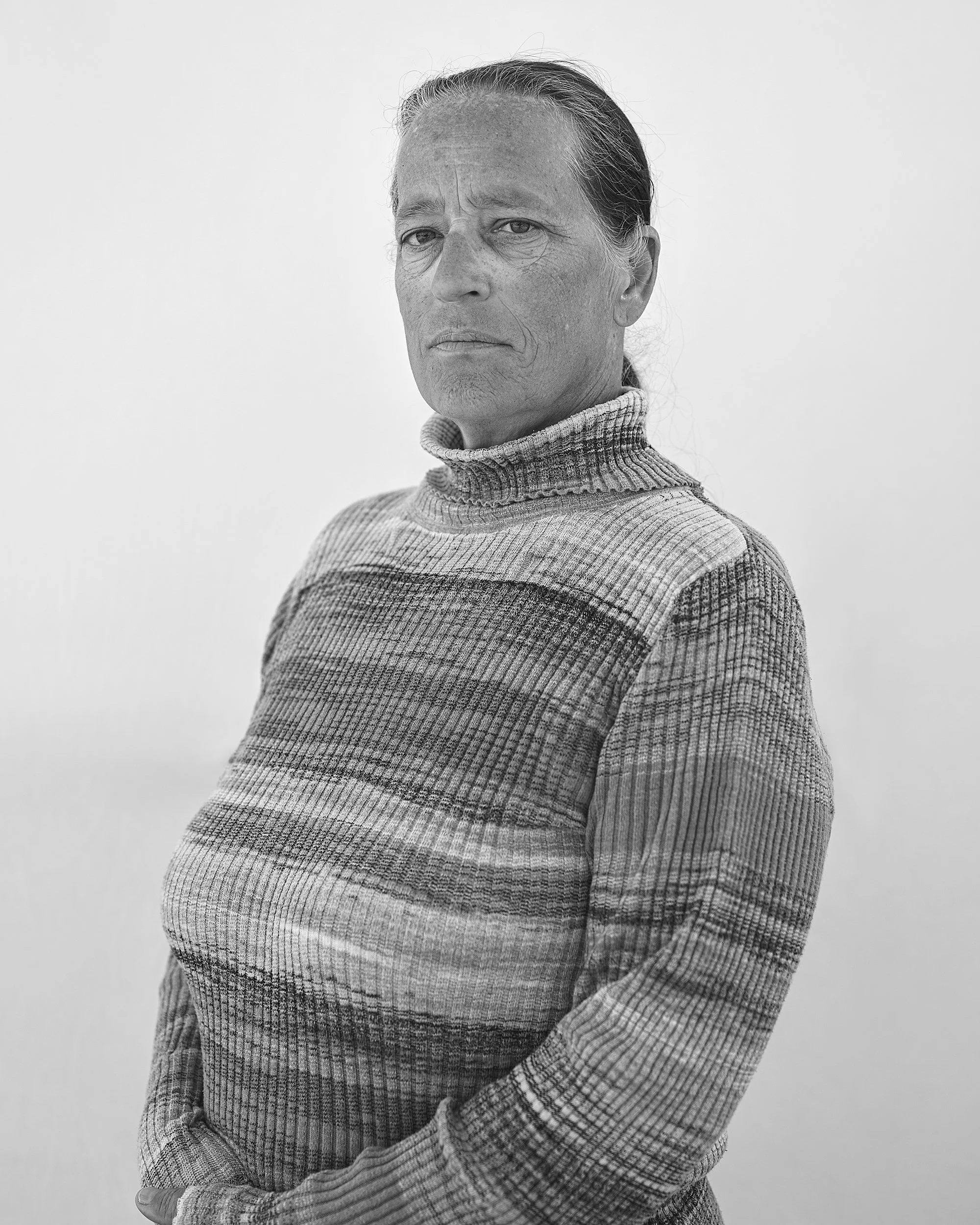 A black and white documentary portrait of a mother attending the rodeo in South Dakota, capturing a candid, quiet moment in the crowd.