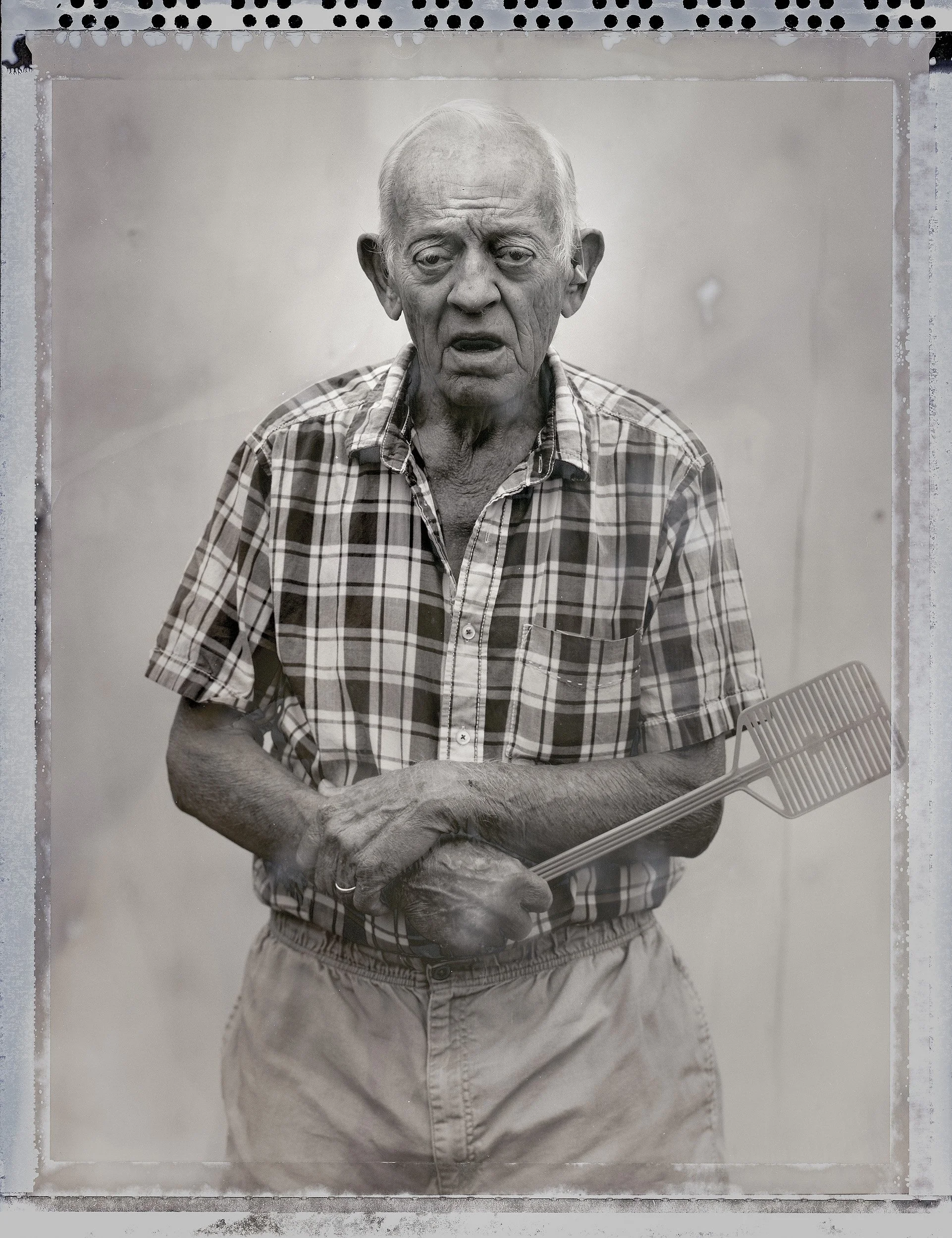 Stark 8x10 large format film portrait of an older man in a plaid shirt holding a fly swatter in Southern Ohio by Parker J Pfister