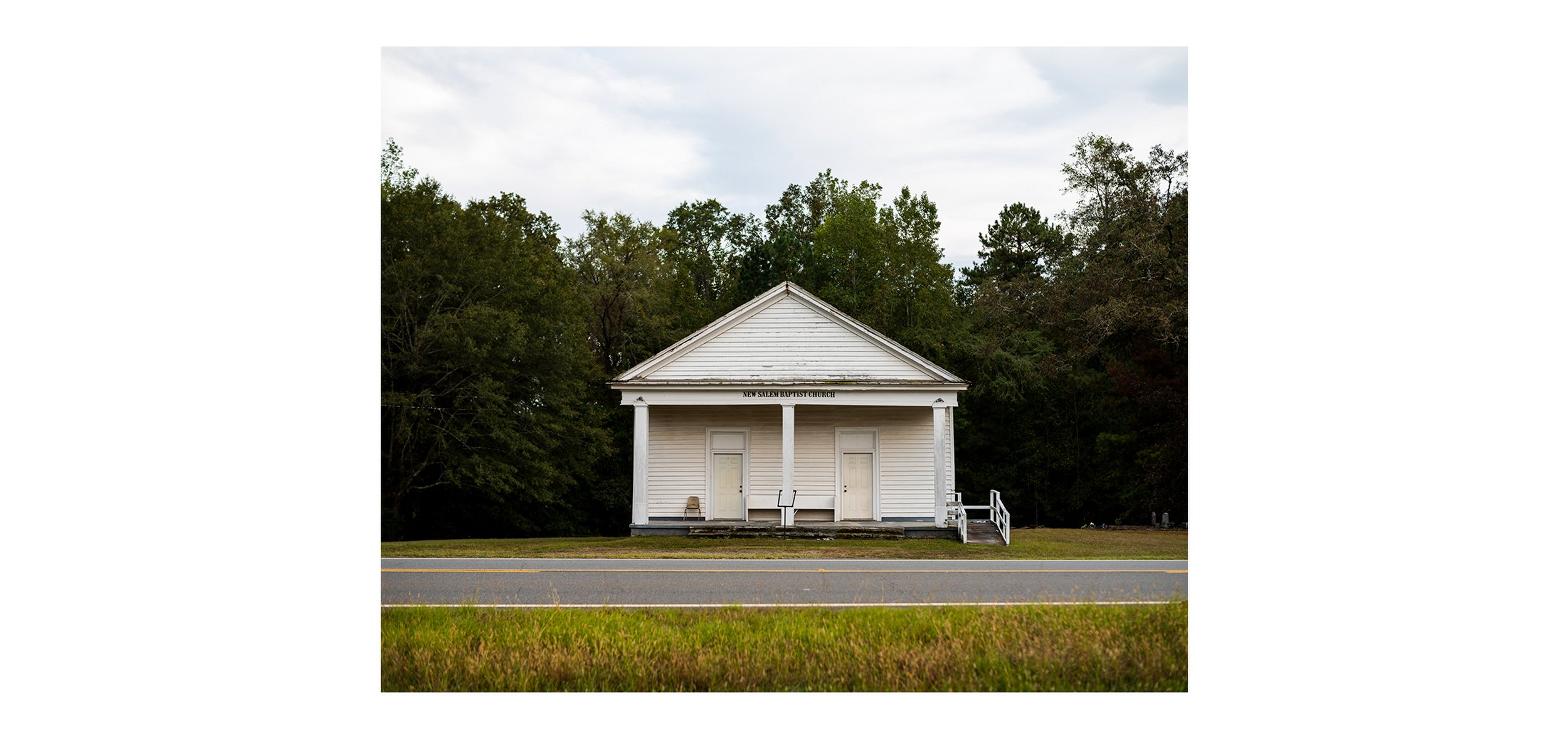 A color documentary photograph of the white New Salem Baptist Church building sitting empty along the roadside, from the Connecting Hwy 80 photography project by Parker J Pfister.