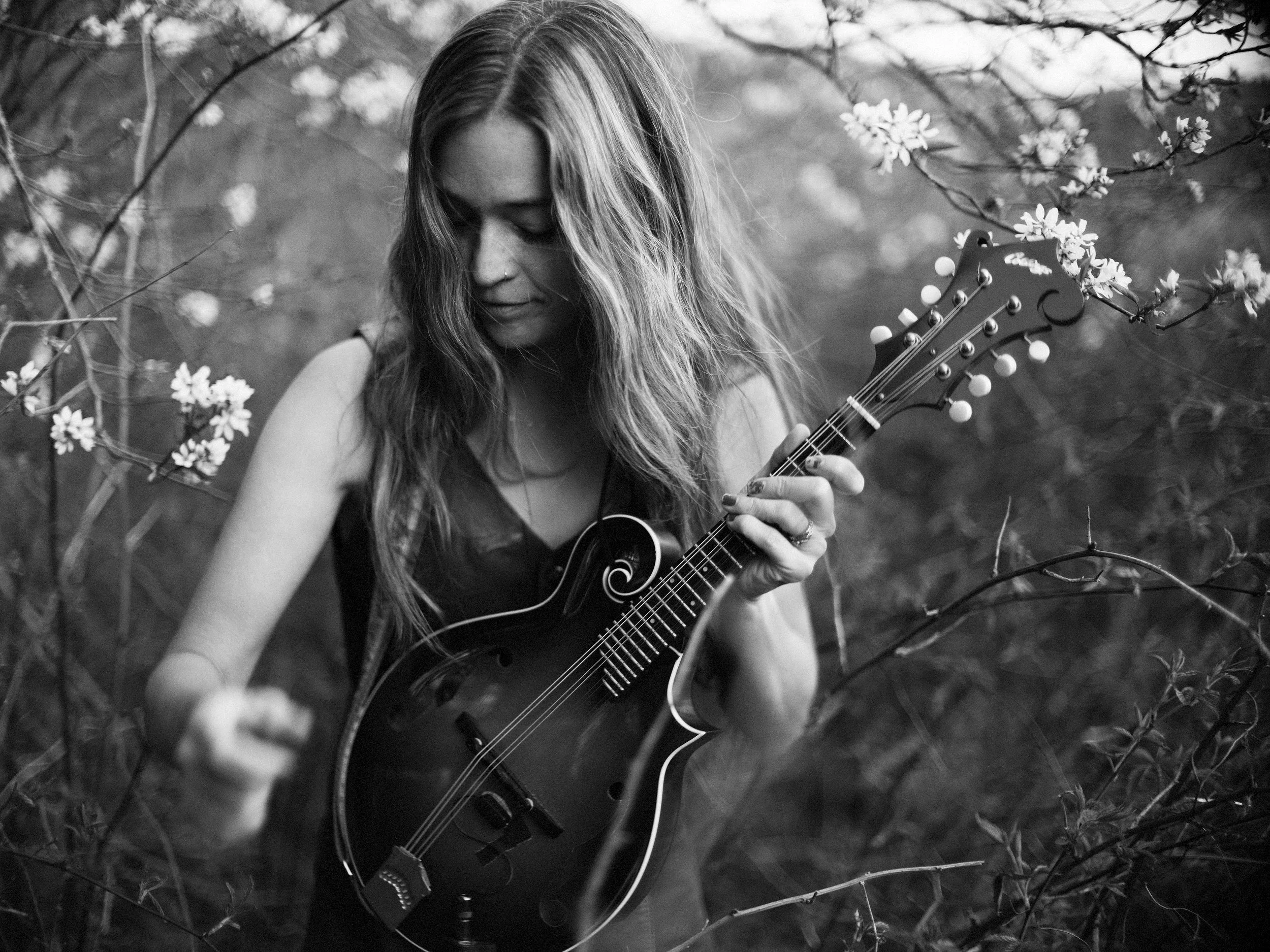 Black and white portrait of musician Lindsay Wall, lead singer of Western North Carolina band Blue Ridge Betty, playing mandolin among blooming trees, photographed by Parker J. Pfister.