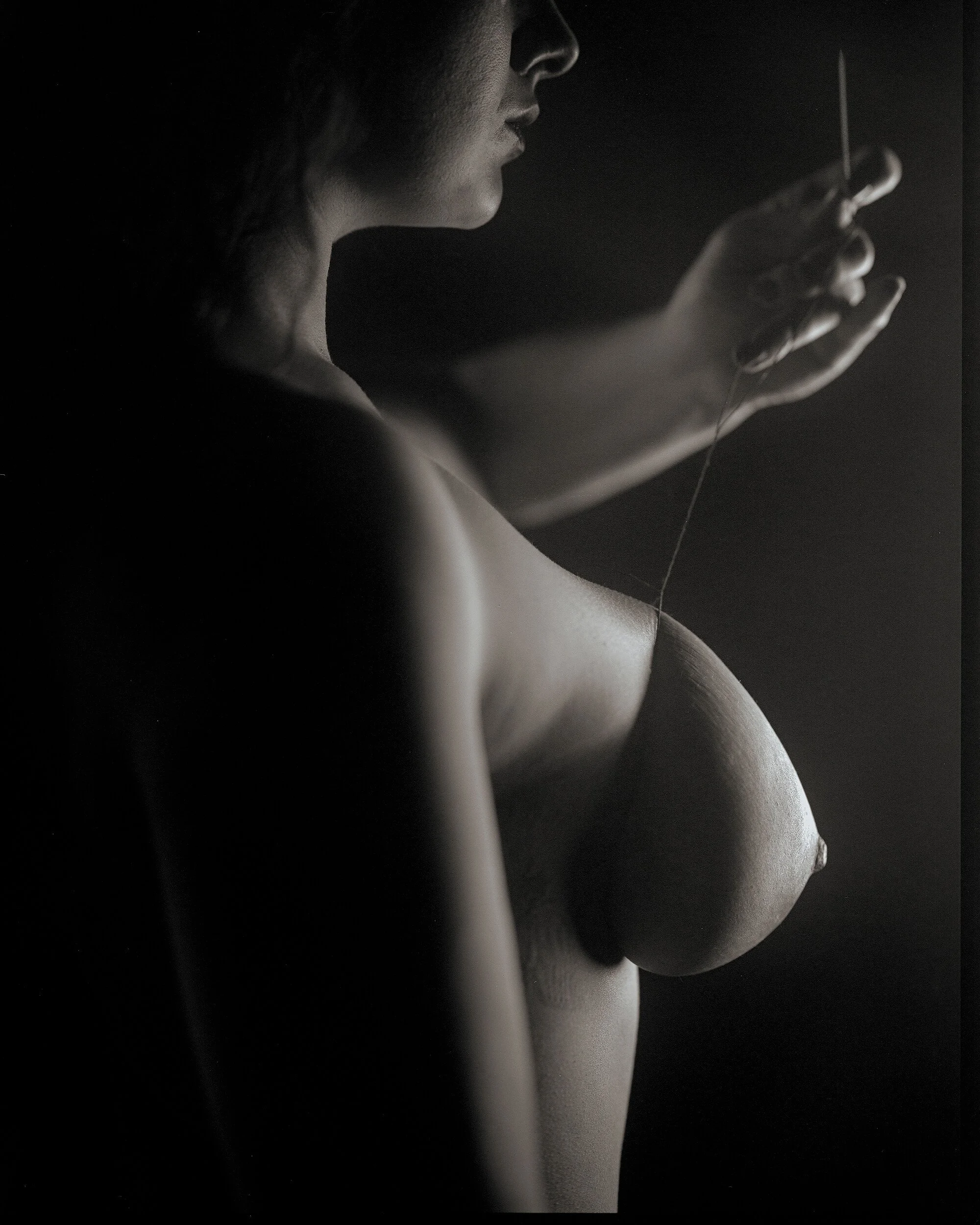 Parker J Pfister Fine Art Black and White Constraint Portrait of a nude white woman with a thread wrapped around one breast and attached to a needle.