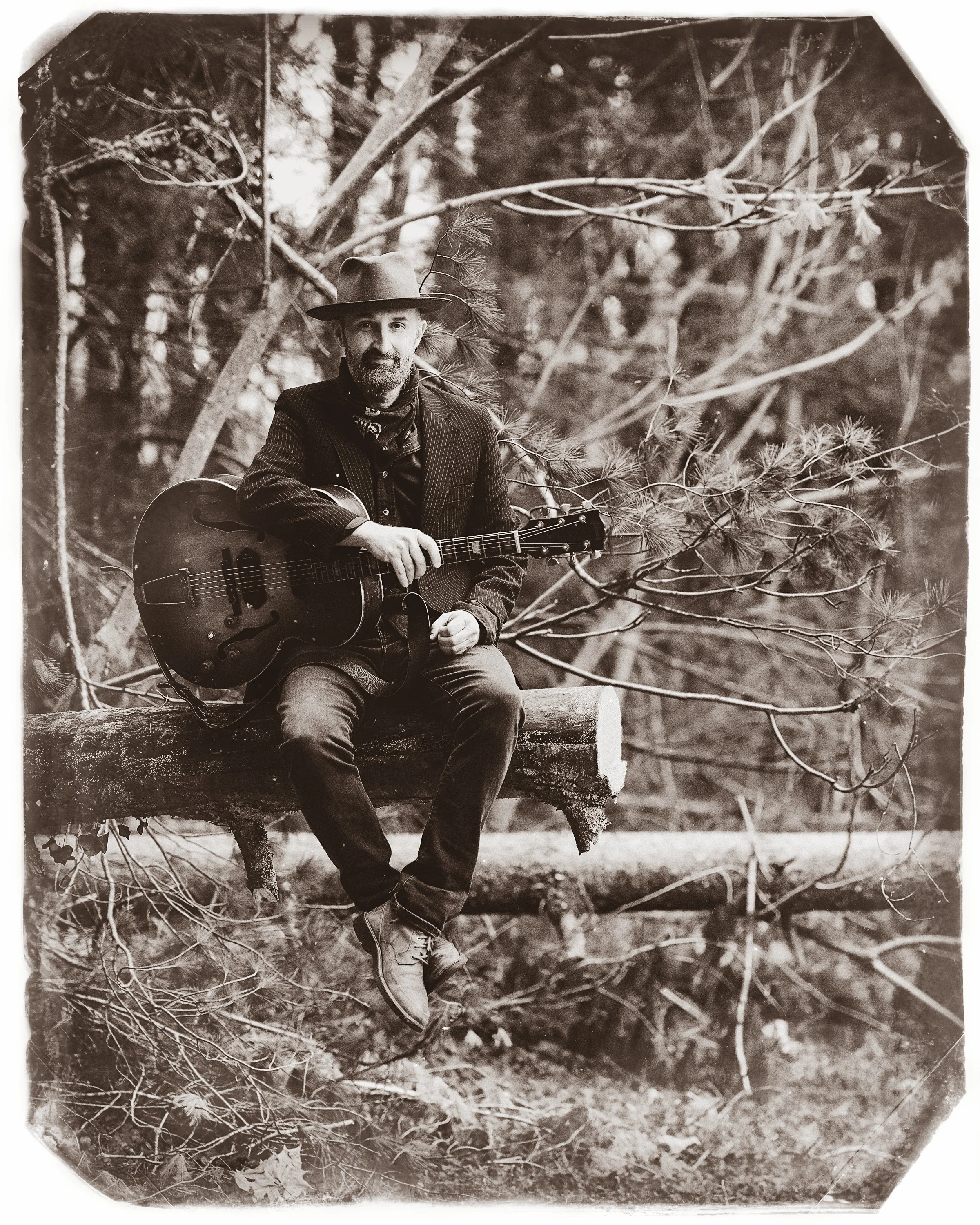 Tinted fine art portrait of blues singer-songwriter Seth Walker seated outdoors in a hat holding an acoustic guitar, captured on film by Parker J. Pfister.