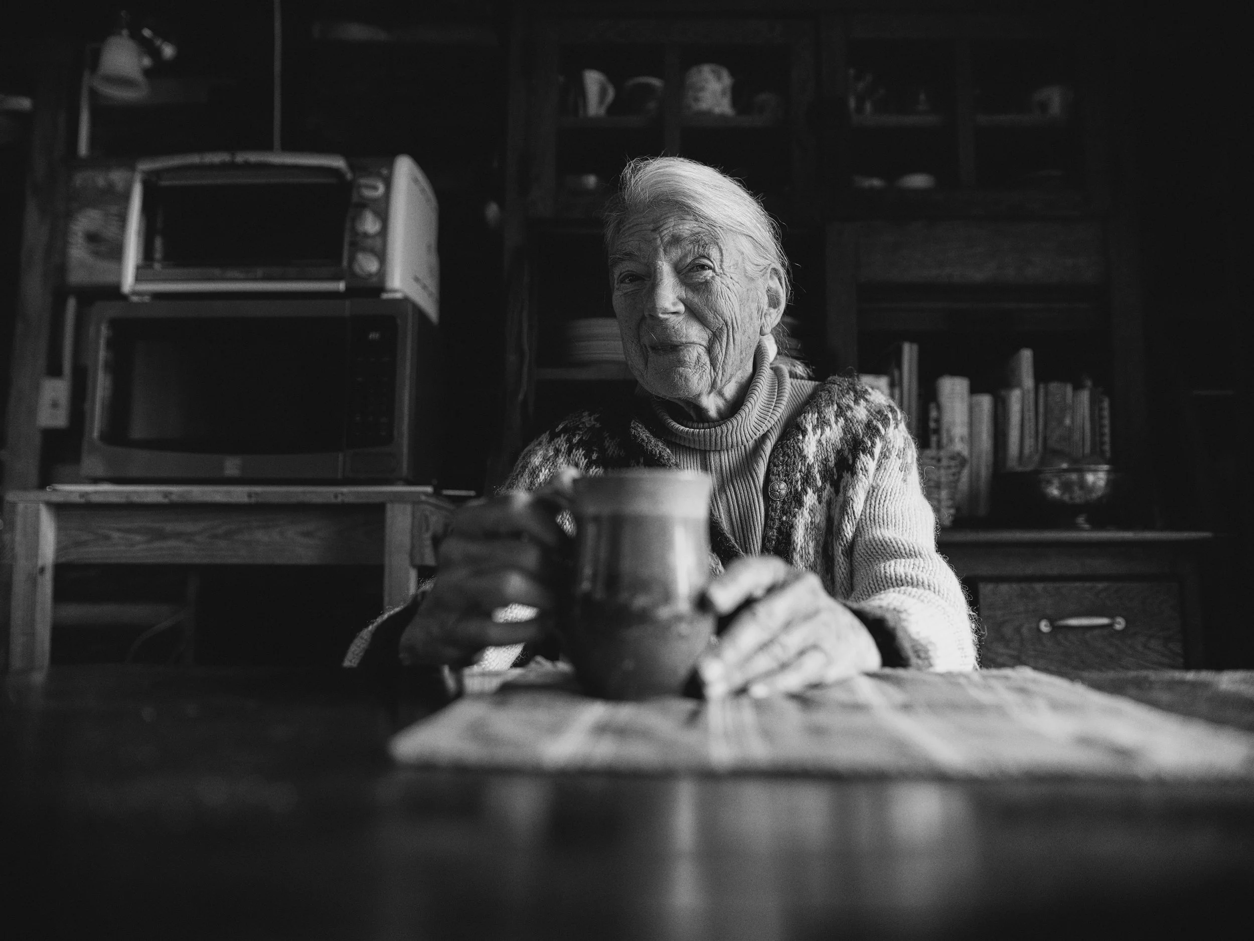 Black and white large format portrait of an elderly woman holding a mug at a wooden table in Madison County NC by Parker J Pfister