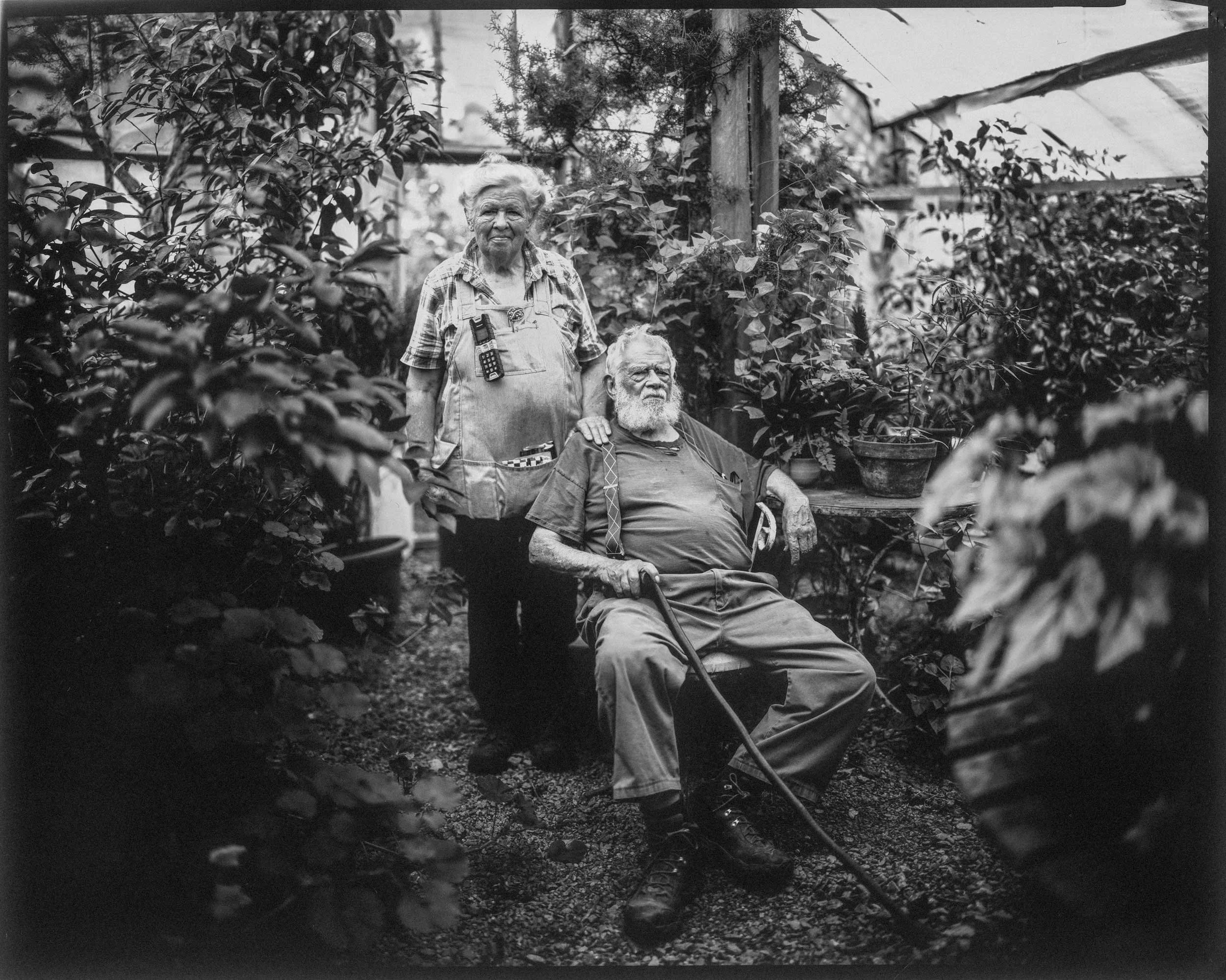 Black and white documentary portrait of an elderly man sitting with a wa