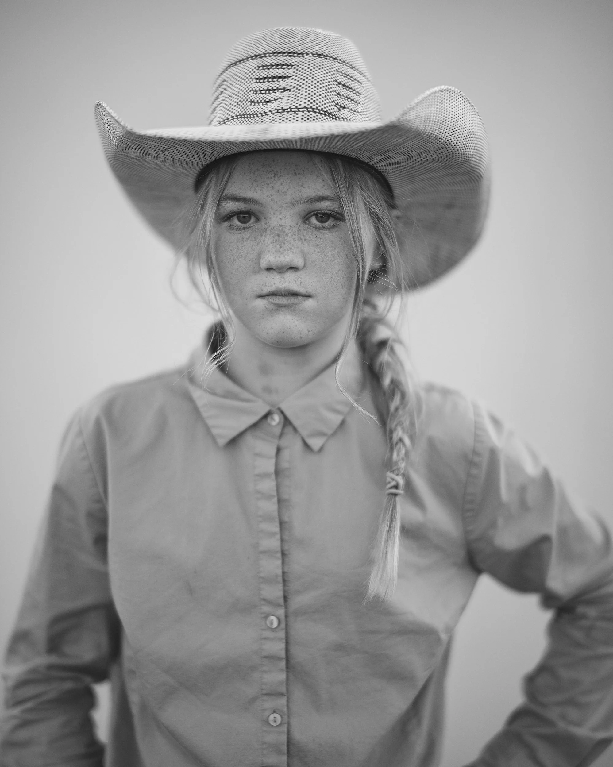 A high-contrast black and white documentary photograph capturing a young girl barrel racer at the Madison County rodeo in North Carolina.