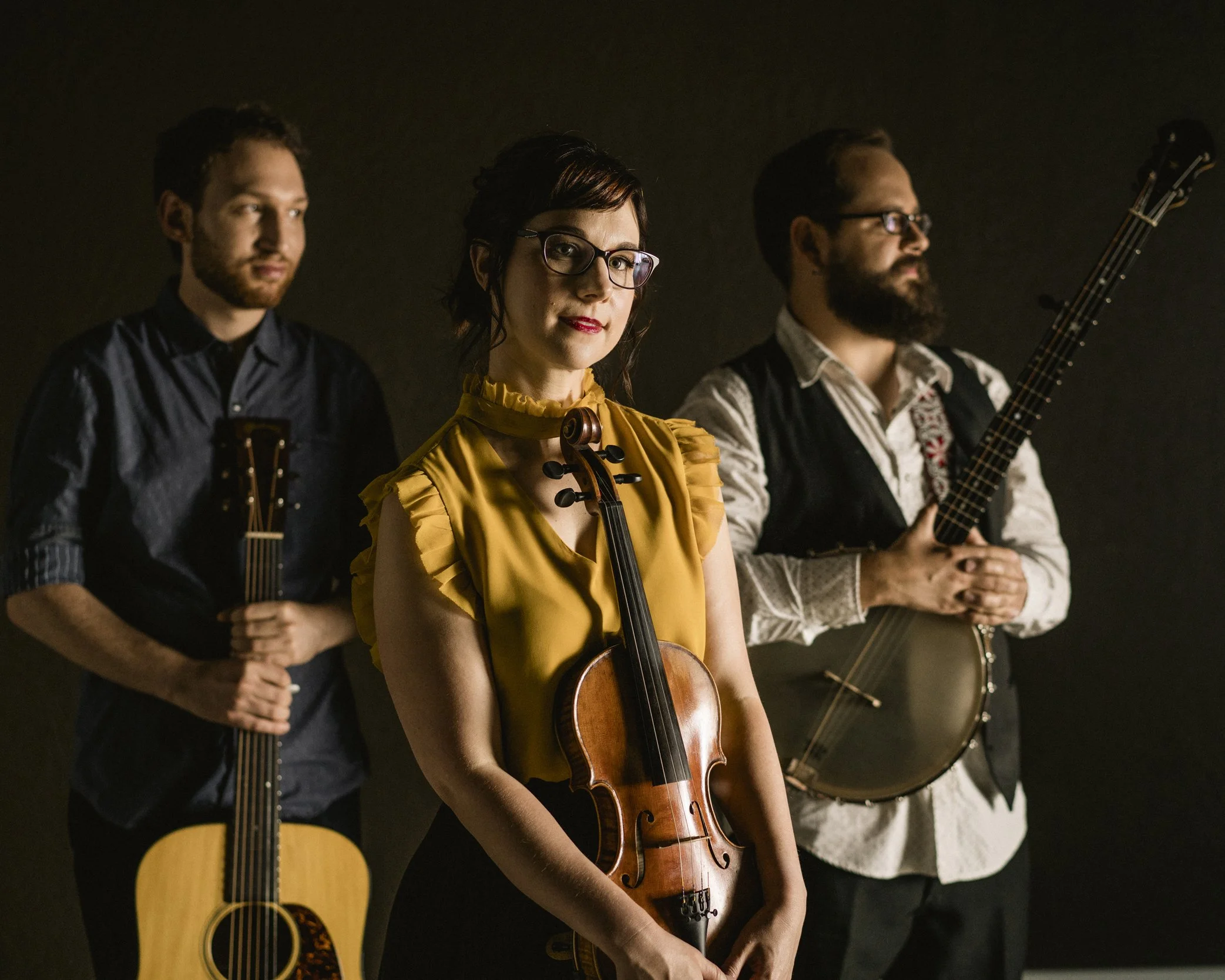Color portrait of Canadian fiddler, singer, and stepdancer April Verch with her bandmates standing together with acoustic guitar, violin, and banjo, photographed by Parker J. Pfister.