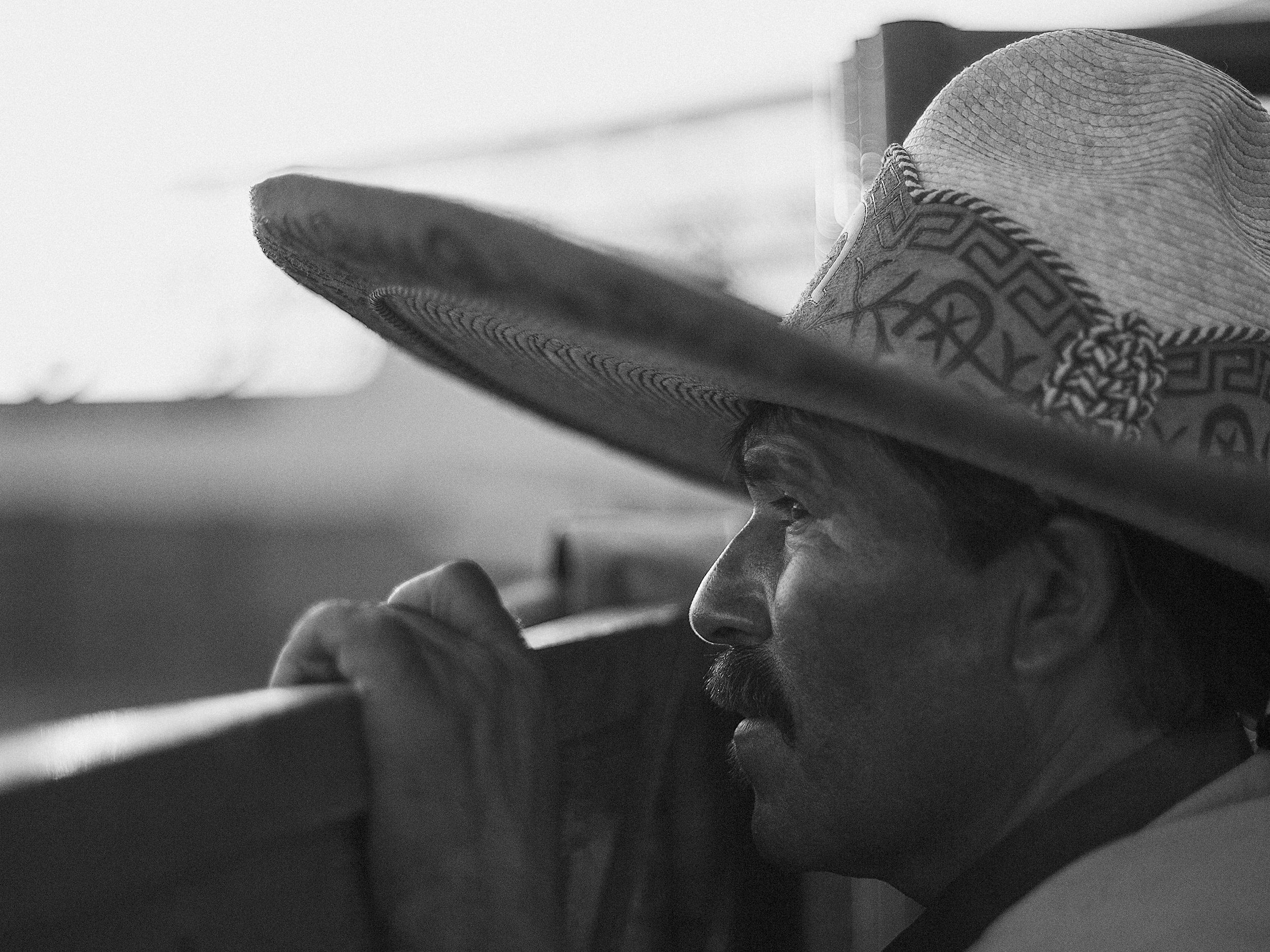 A portrait-heavy documentary frame showcasing the quiet gravity and raw likeness of the arena hands working the pens during a traditional rodeo in Mexico.