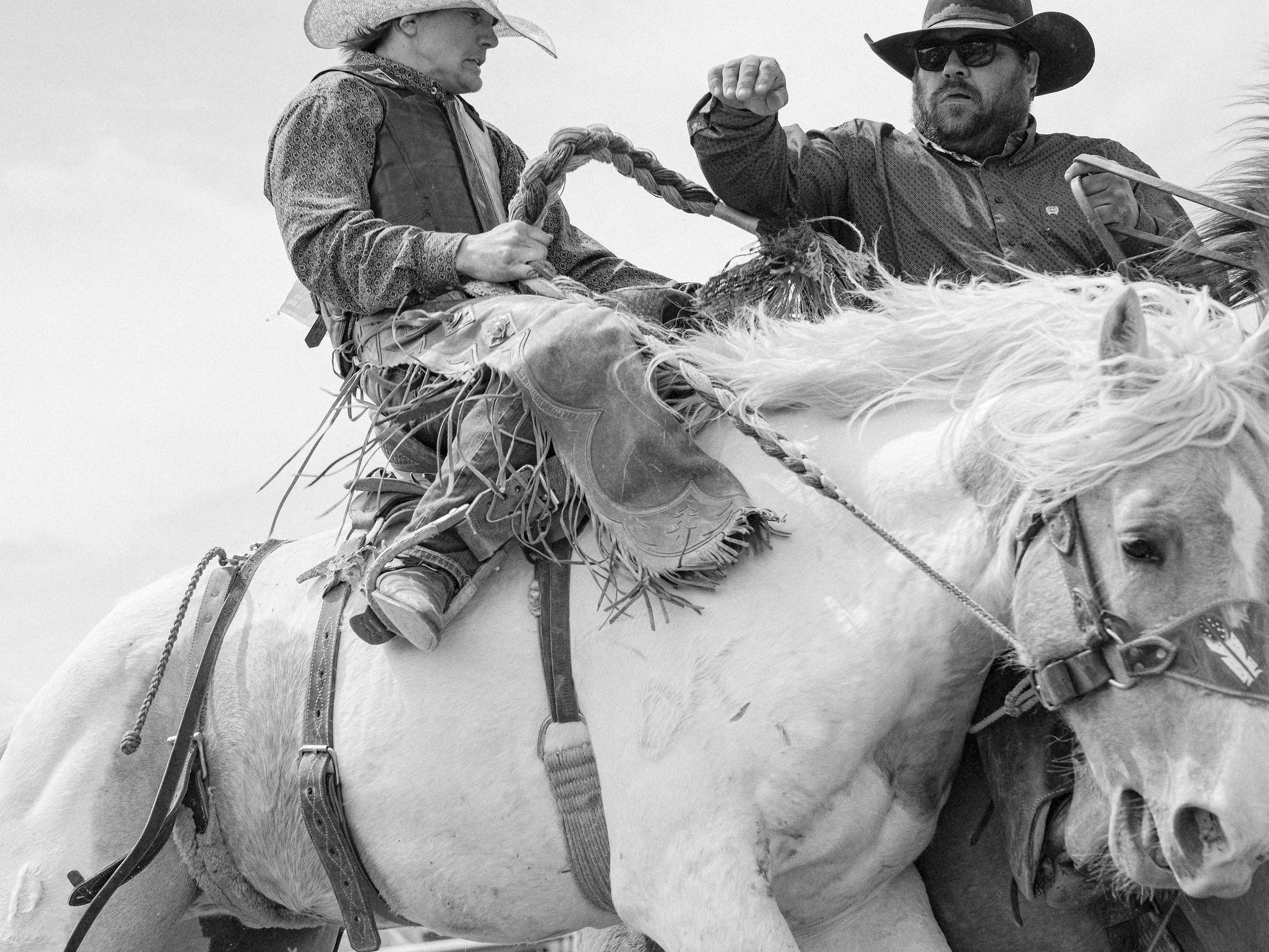 A first-person documentary photograph from the dirt behind the chutes at a South Dakota rodeo, capturing the fleeting presence and atmosphere of the arena.