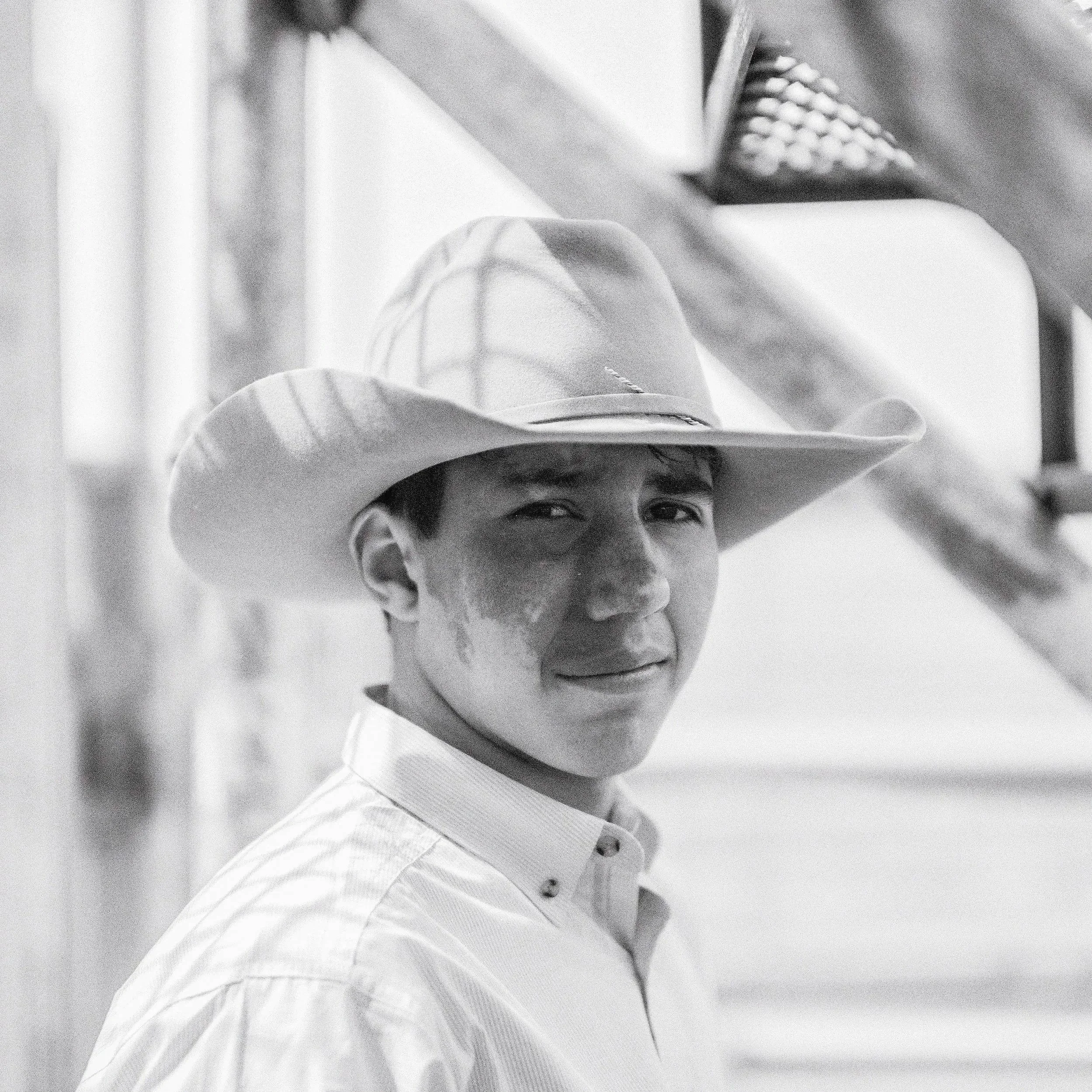 A raw, high-contrast black and white documentary photograph capturing the fleeting presence and quiet gravity of riders behind the chutes in Philip, South Dakota.