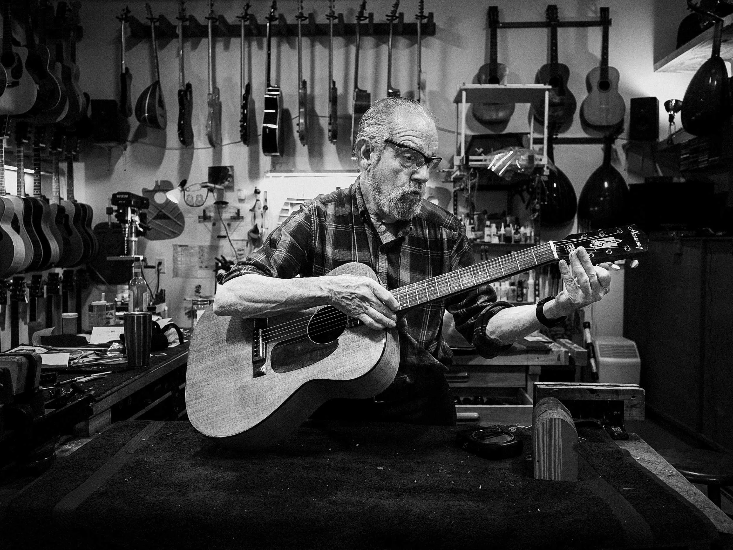 Black and white portrait of custom instrument luthier Harry Norris seated in his workshop holding an acoustic guitar, photographed in Western North Carolina by Parker J. Pfister.