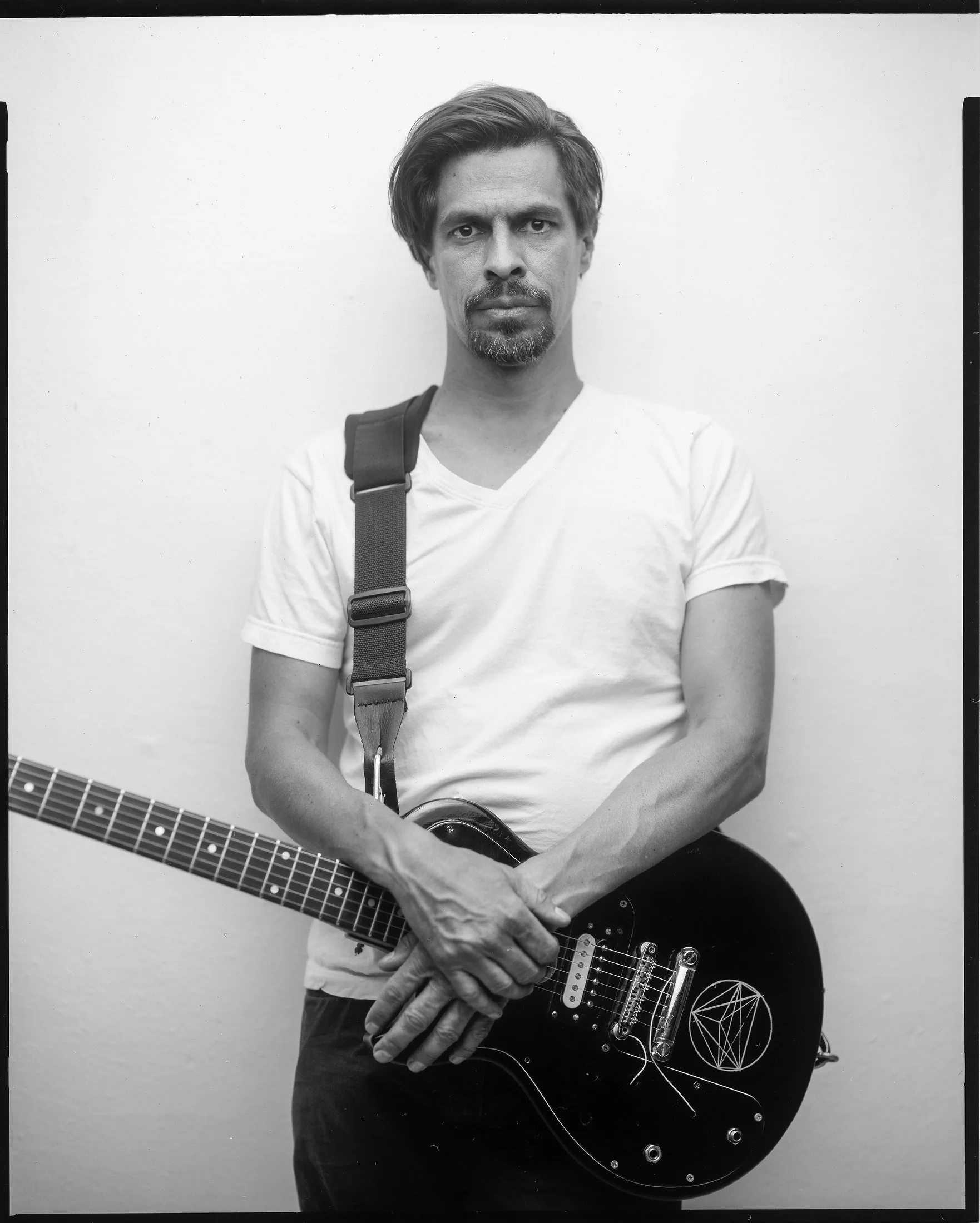 Clean studio portrait of guitarist Raven Tenderfoot standing with an electric guitar, photographed by Parker J. Pfister.