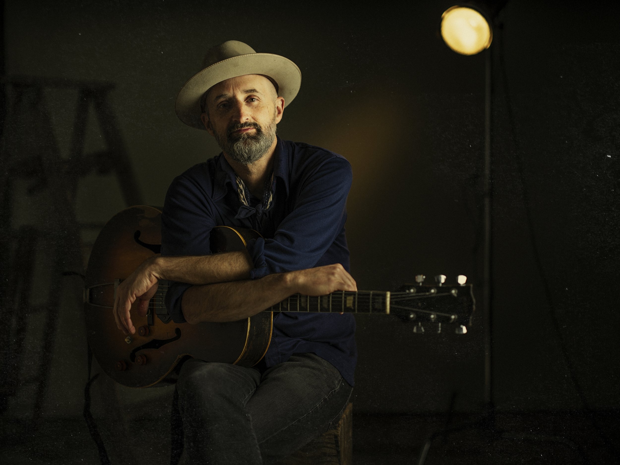 Warm indoor portrait of blues musician Seth Walker playing guitar under soft stage lighting, photographed by Parker J. Pfister.