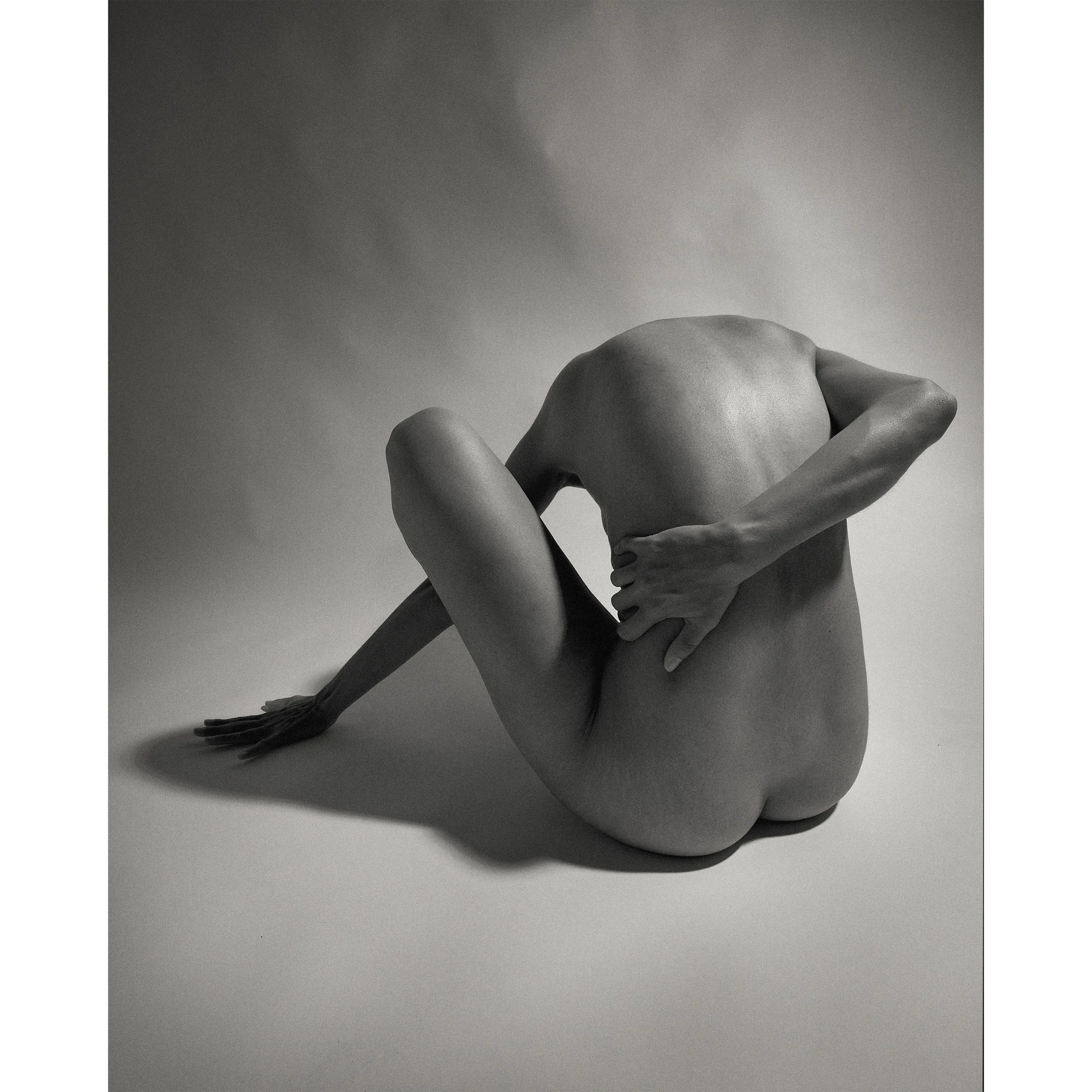 The composition captures a beautifully sculpted, seated nude human form against a clean, empty background, highlighting the curves of the back and limbs to convey a sense of introspection and resilience.