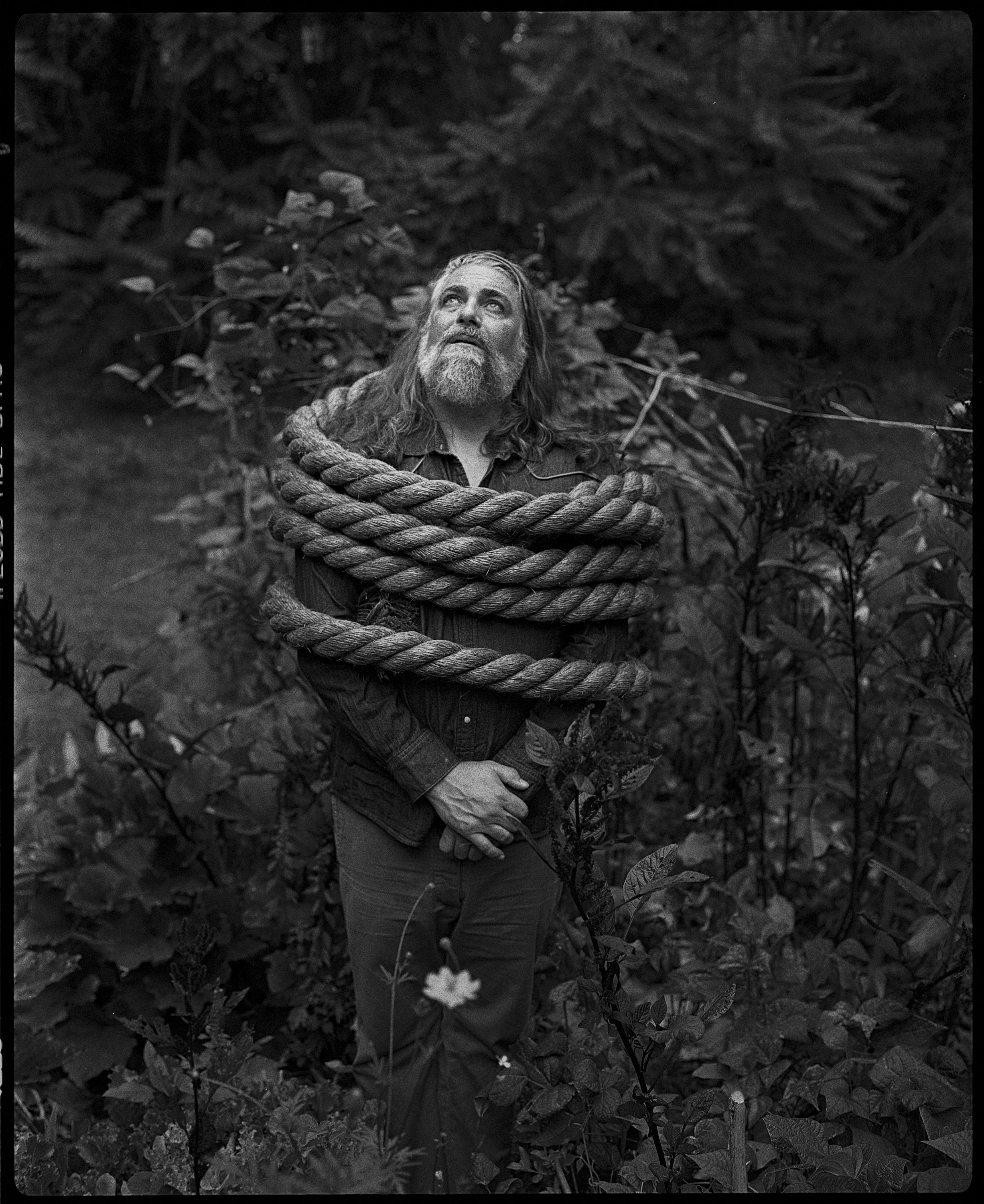 Black and white portrait of musician The White Buffalo wrapped in rope in a forest, captured on film with a Plaubel Makina 67 camera by Parker J. Pfister in Asheville, NC.