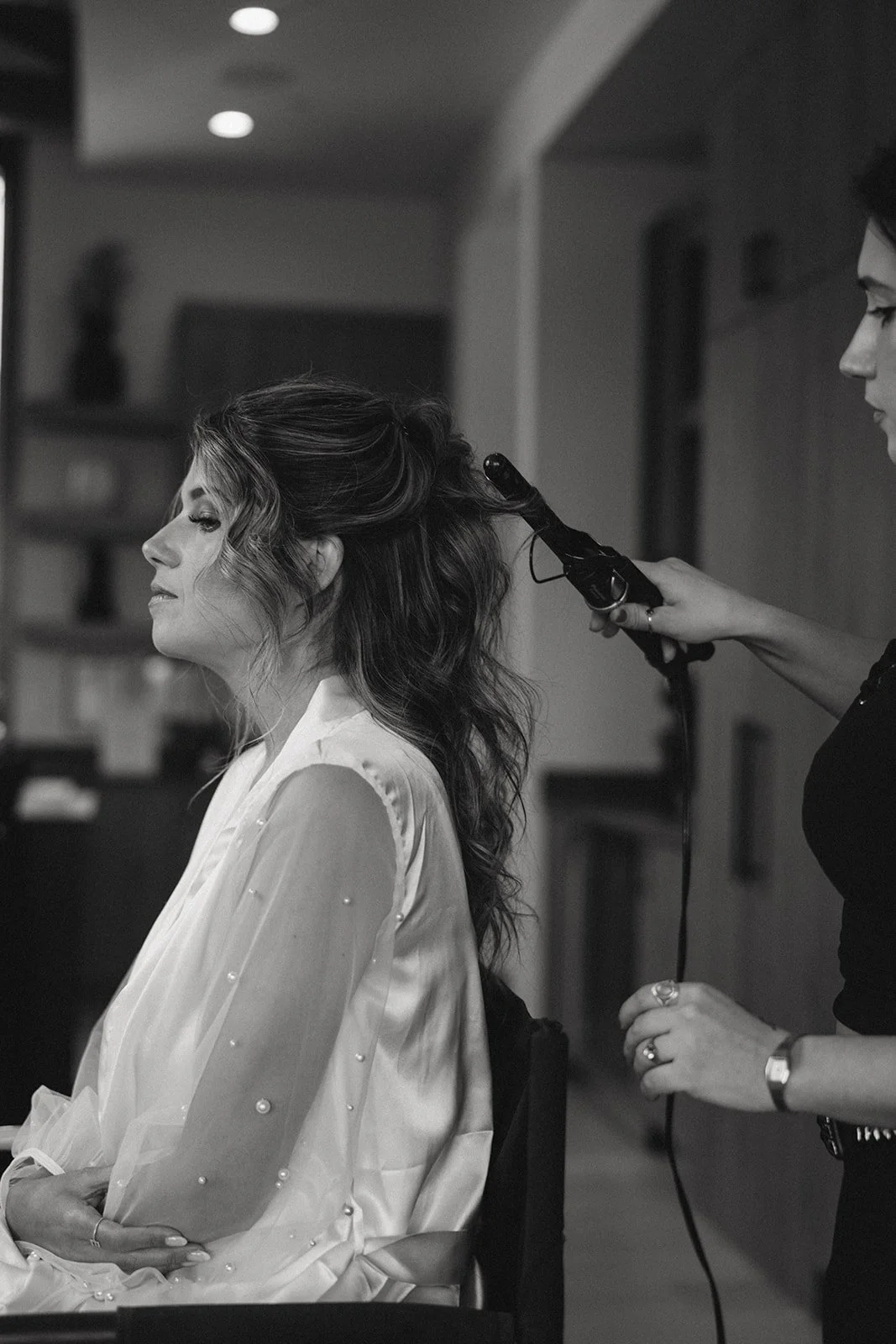 A woman is getting her hair styled with a curling iron by a stylist in a salon or makeup studio.